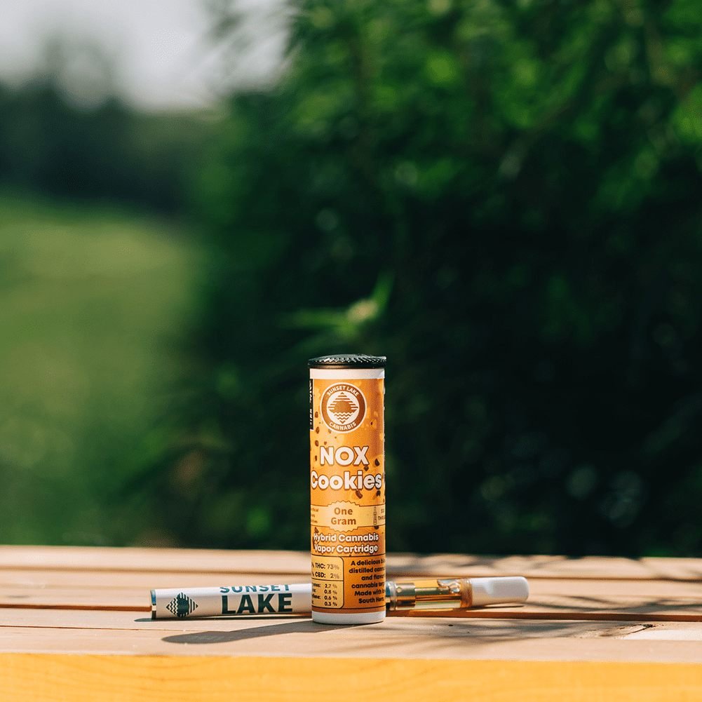 Photo of a Sunset Lake Cannabis NOX Cookies vape cartridge and battery sitting on a wooden crate in a cannabis field.