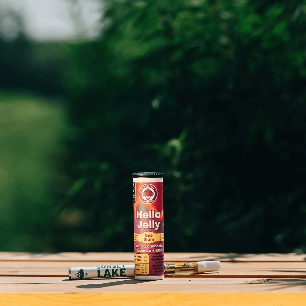 Photo of a Sunset Lake Cannabis Hella Jelly vape cartridge and battery sitting on a wooden crate in a cannabis field.