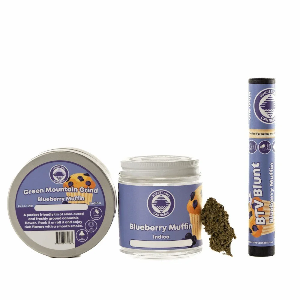 Photo of Sunset Lake Cannabis Blueberry Muffin strain products including a tin of Green Mountain Grind, a quarter ounce jar of hand-trimmed flower, a loose bud, and a BTV Blunt.