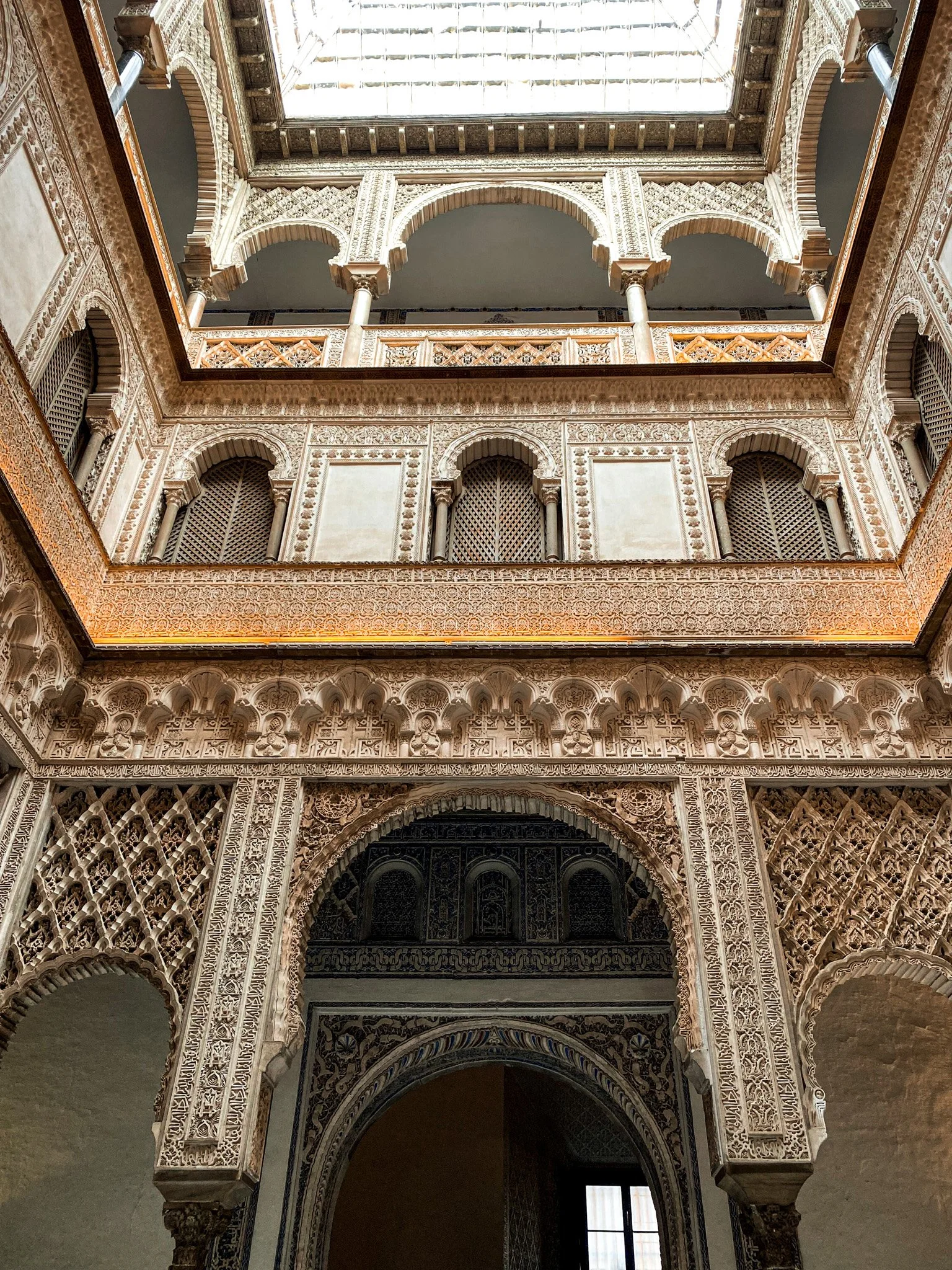 Interior of a historic building with intricate Islamic-style architectural details, including ornate arches, carved stucco, and a large central skylight.