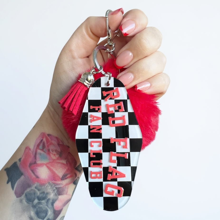 Red Flag Fan Club Motel Keychain by the Bitter Bitch Coin black and white checkers with a red leather tassle and oversized pompom