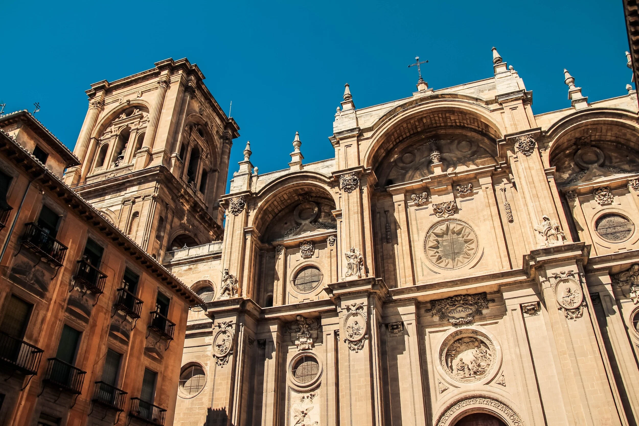 View of an ornate historical cathedral with detailed sculptures, arches, and a clock, against a clear blue sky.