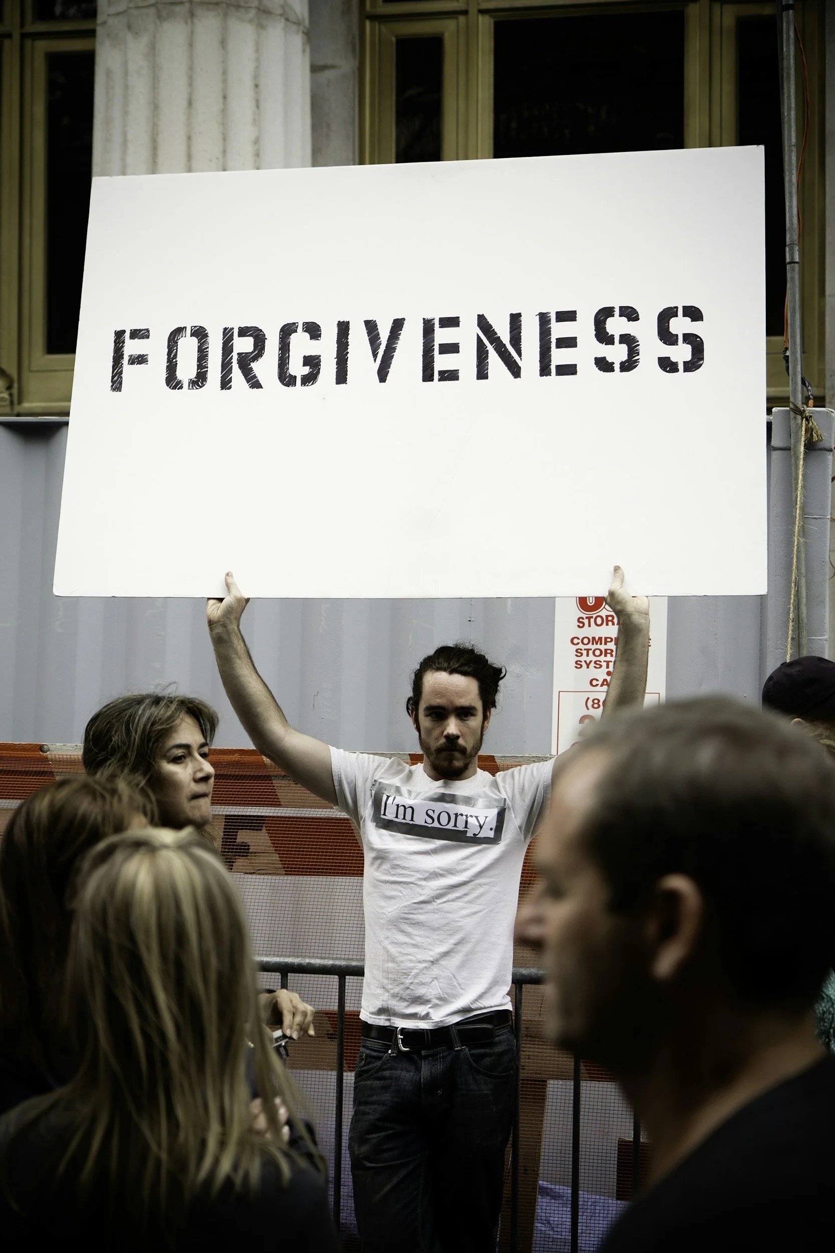 The Bitter Bitch Lifestyle Blog: Forgiveness.  A man with a sign that reads "forgiveness" stands on the sidewalk with "I'm sorry" taped to the front of his shirt with duct tape.
