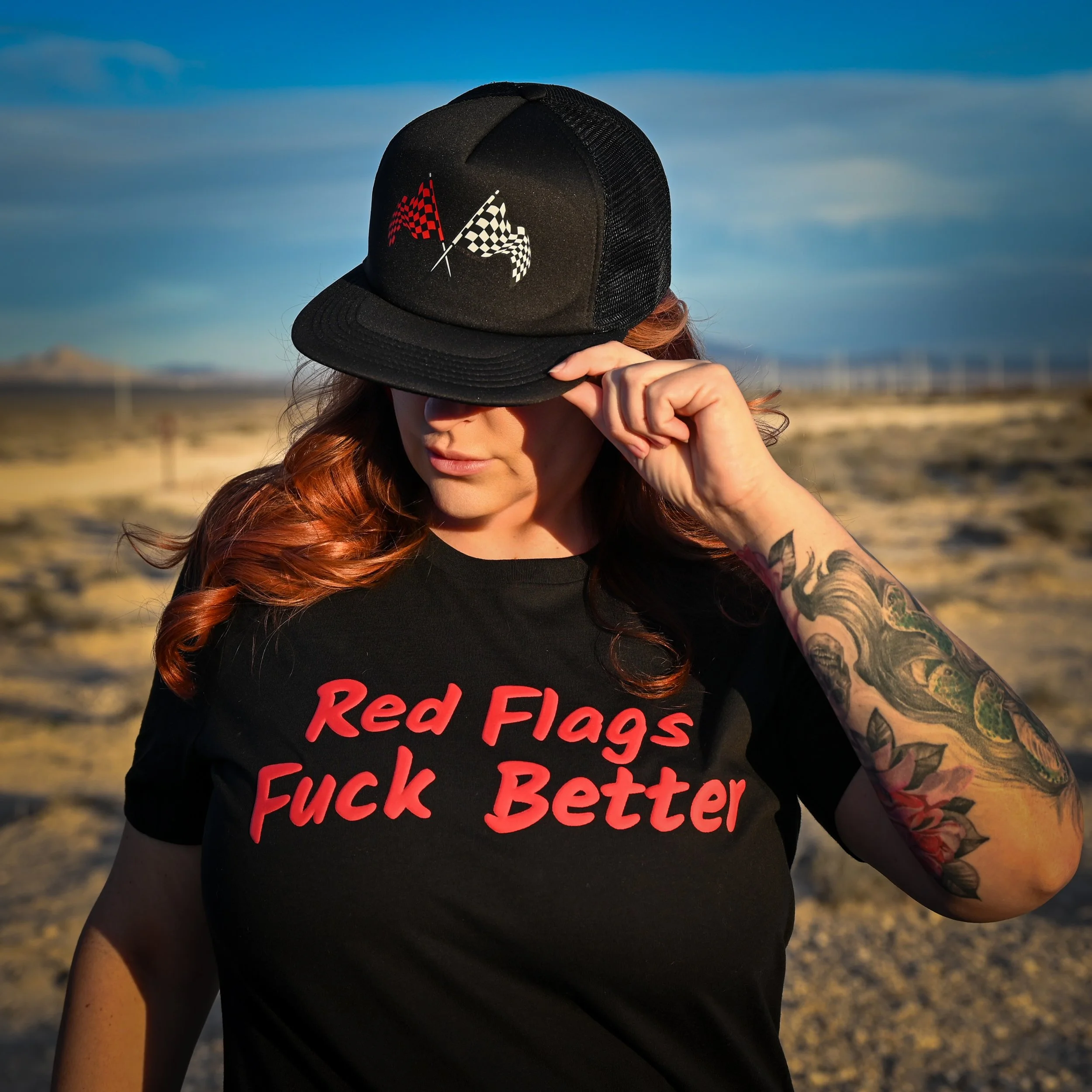 Red Flags Fuck Better women's puff print tee in black and red with signature checkered flag logo in red and white on a black foam trucker cap by the bitter bitch co