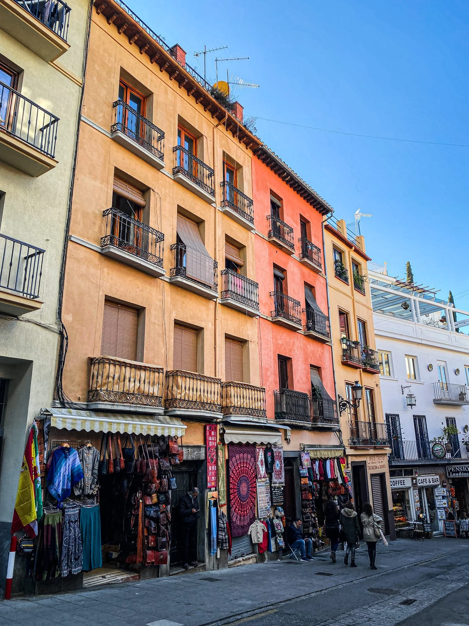 Colorful multi-story building with small street shops on the ground floor and people walking on the sidewalk.
