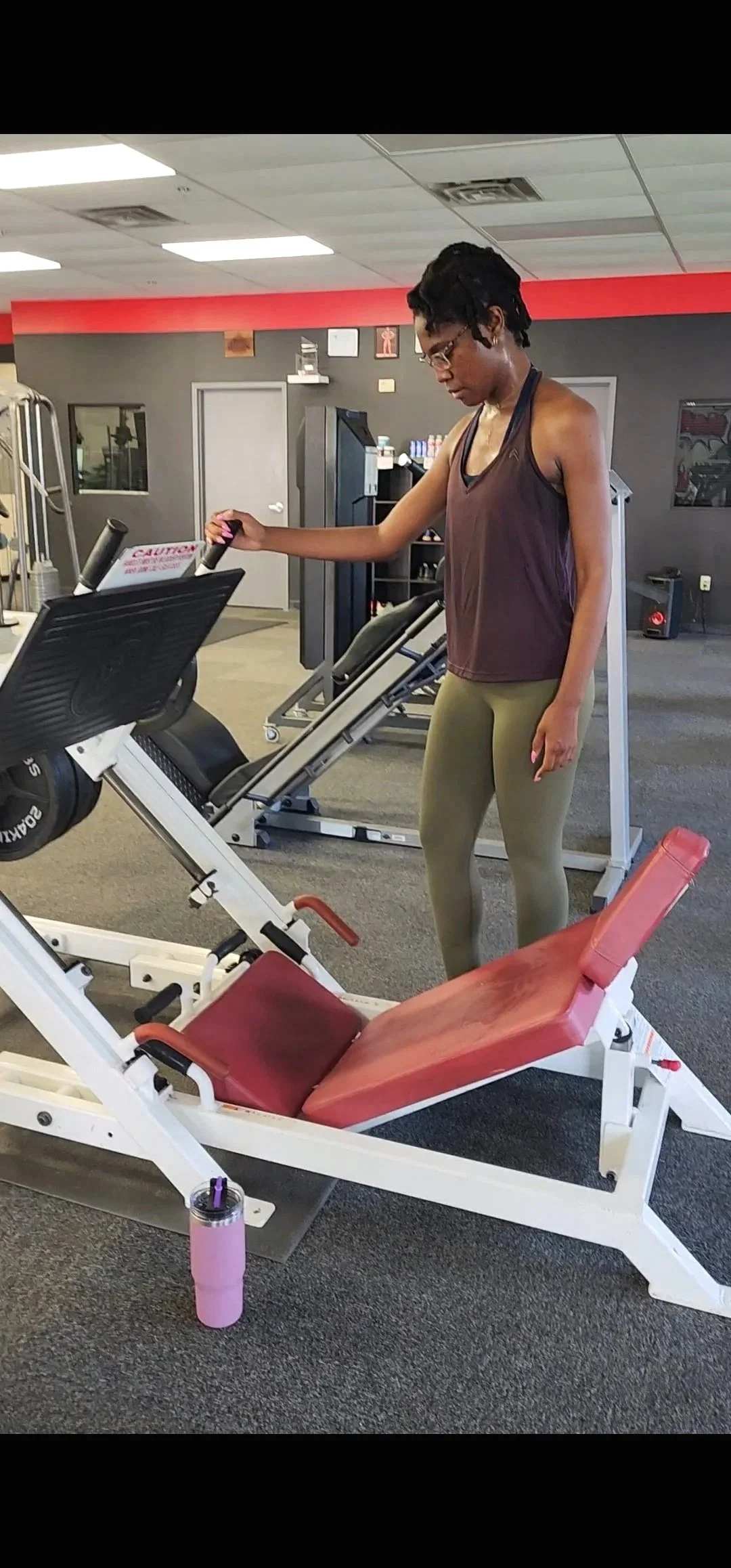 A woman in workout attire standing next to a gym exercise machine, holding onto the machine's handles.