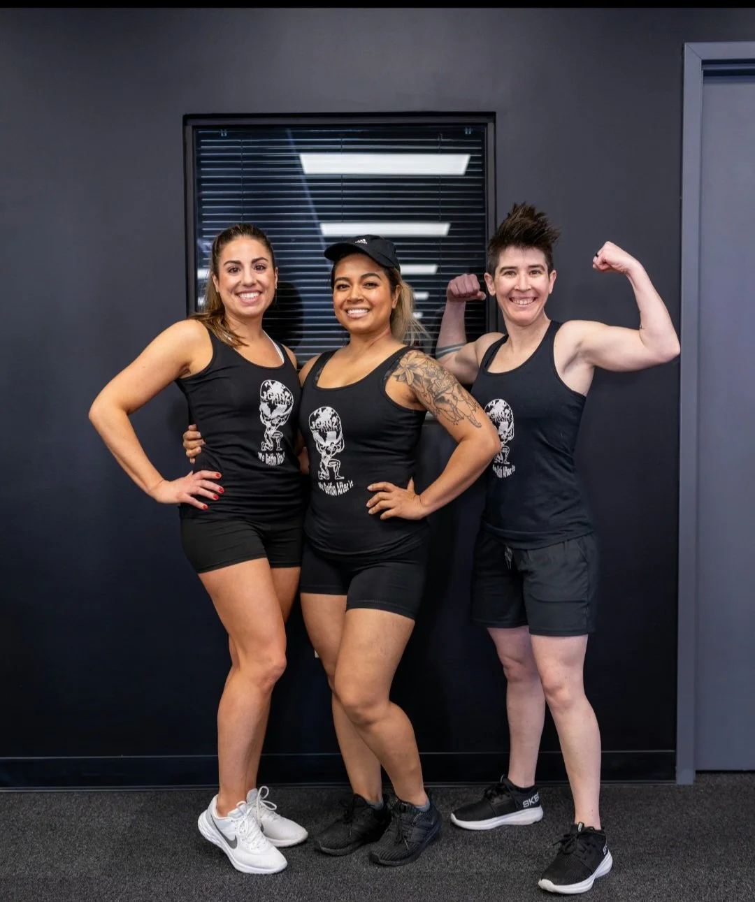 Three women in athletic clothing pose confidently in a gym, showcasing their muscles.