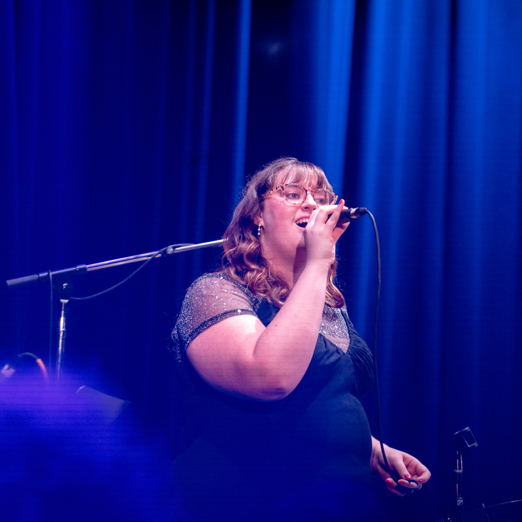 A female singer performing on stage with a microphone, under blue stage lighting.