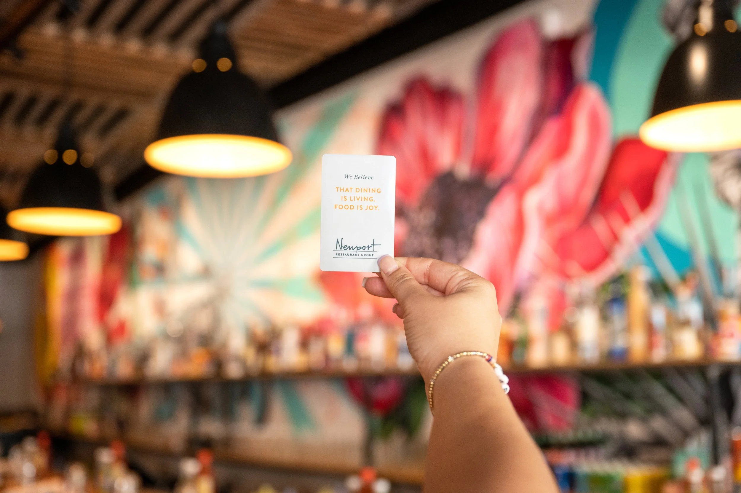 hand holding a gift card with a blurred mural and bar in the background