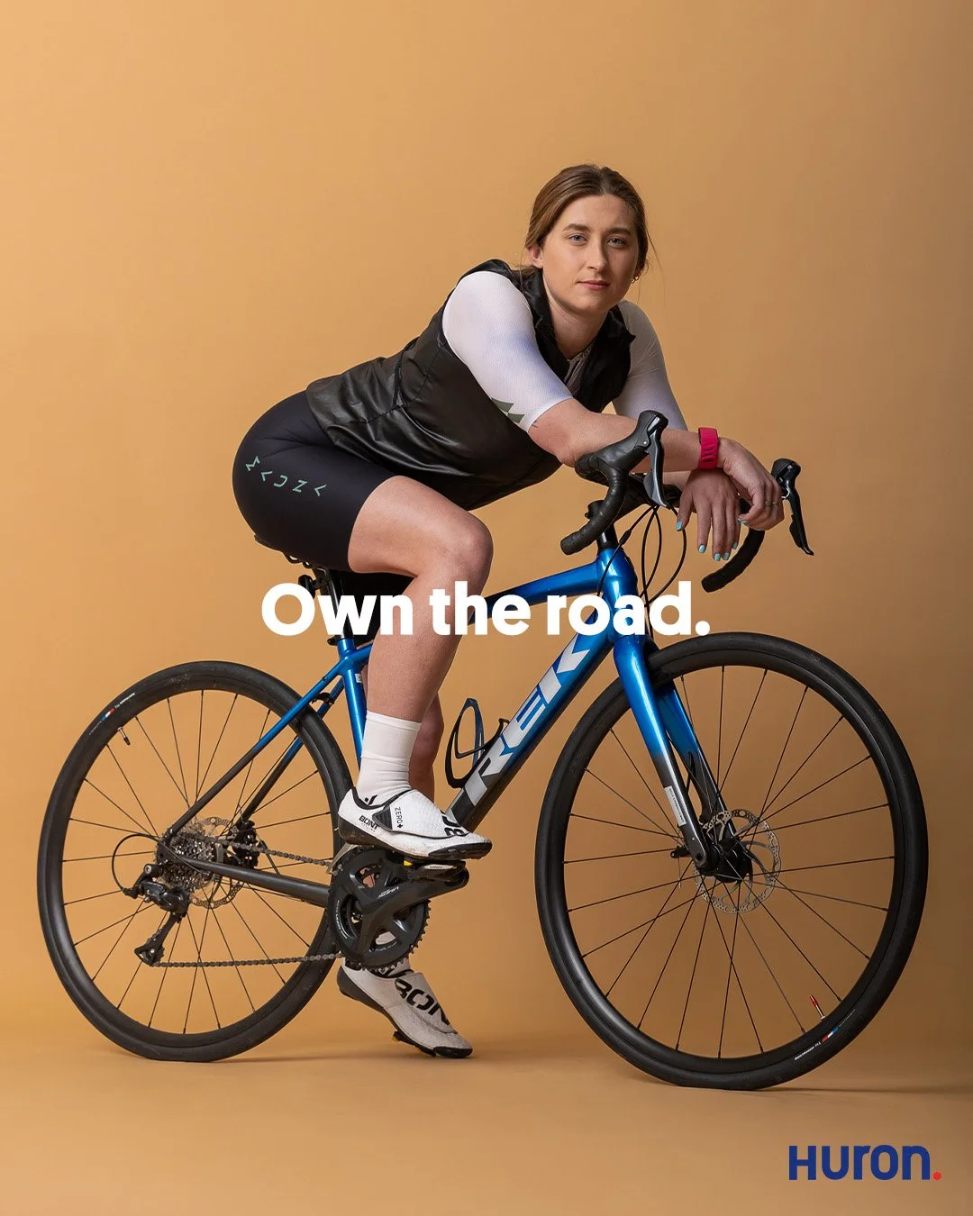 Professional commercial studio photography of a female cyclist with a blue Trek road bike for the Huron campaign. The shot captures a high-end editorial look for athletes, serving as the "before" state in a performance-to-recovery brand story.