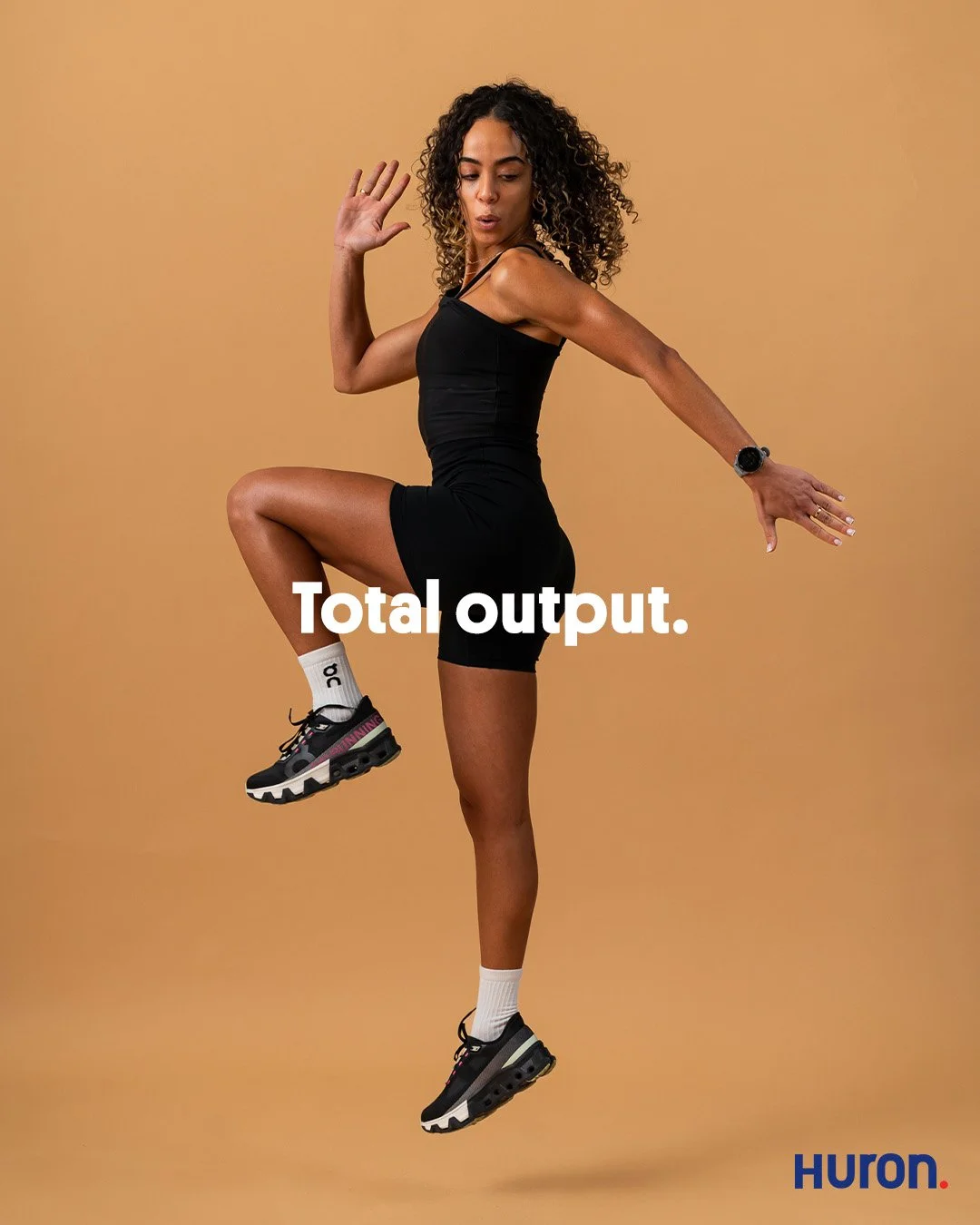 Commercial athletic portrait of a female Pilates athlete in mid-air jumping action. High-end editorial photography for Huron focusing on the go-getter performance state without gritty training content.