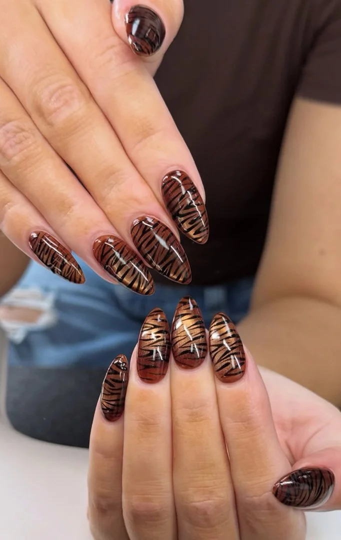 Close-up of a person's hands with tiger stripe nail art on their nails.