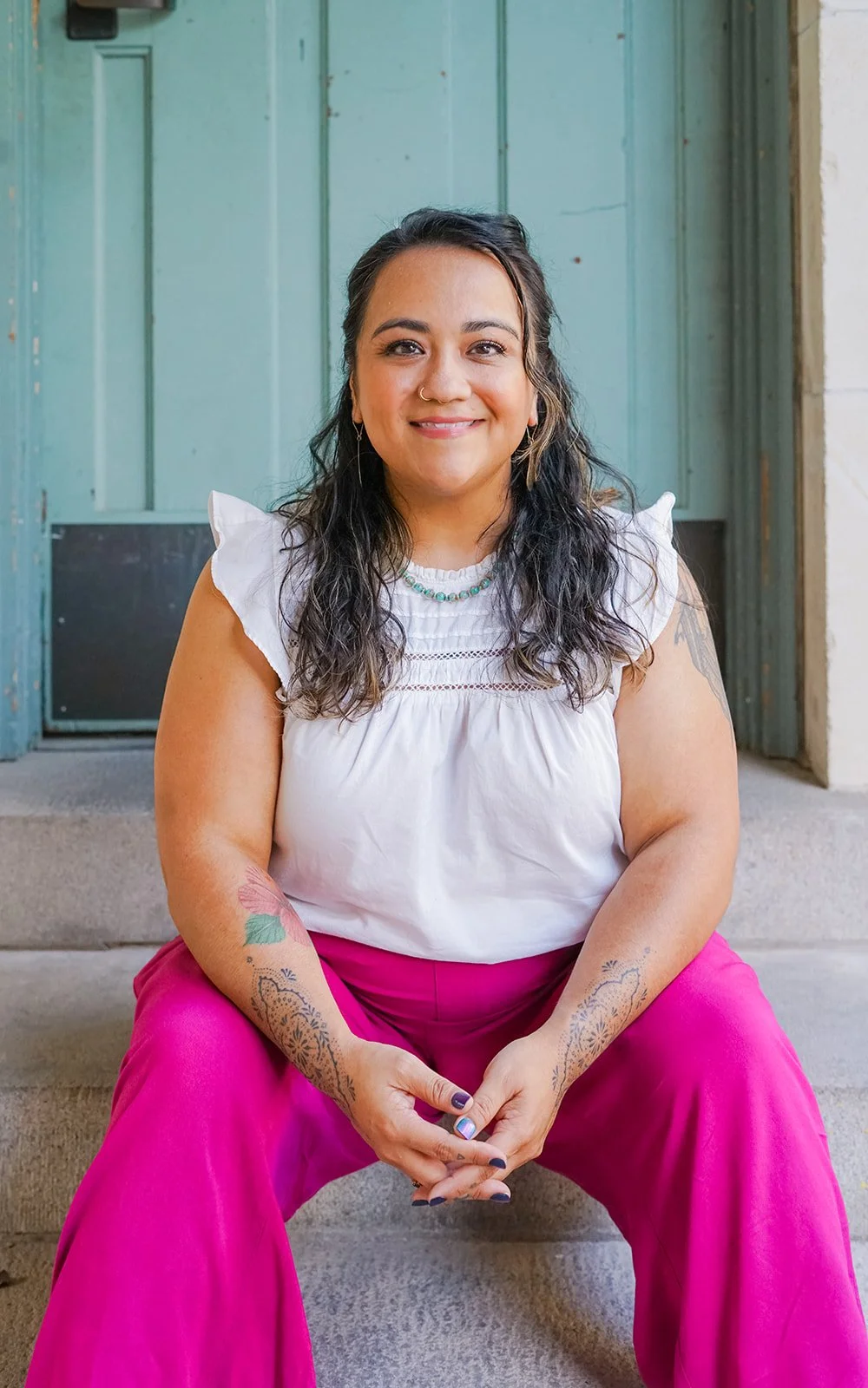 Professional portrait of a woman seated on steps in front of a teal doorway, smiling calmly at the camera
