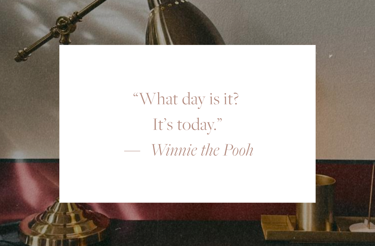 Quote card reading: "What day is it? It's today." — Winnie the Pooh, overlaid on a cosy writing desk with a brass reading lamp, and warm afternoon light.