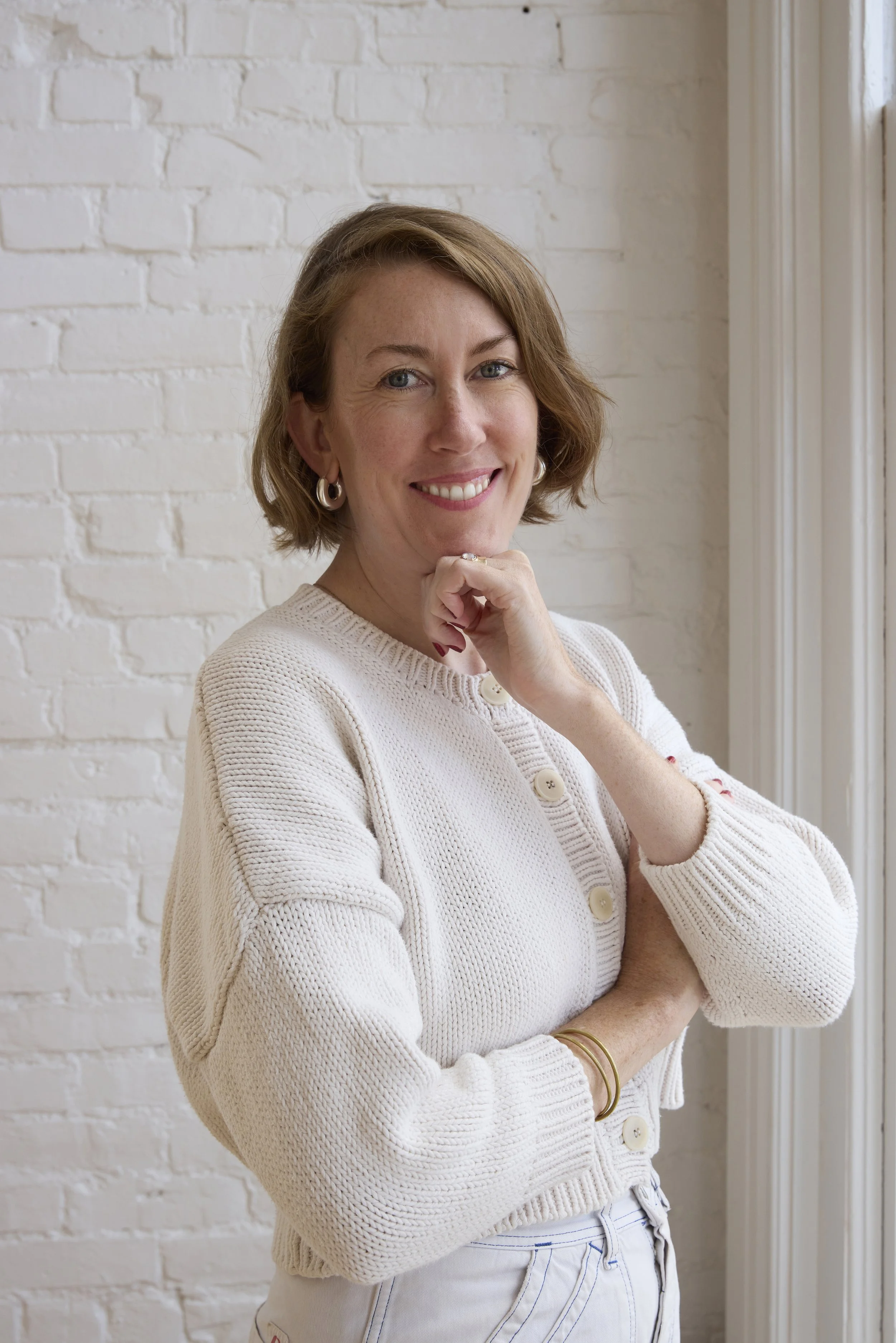 Smiling woman with long brown hair and a fringe, wearing a brown top against a white background.