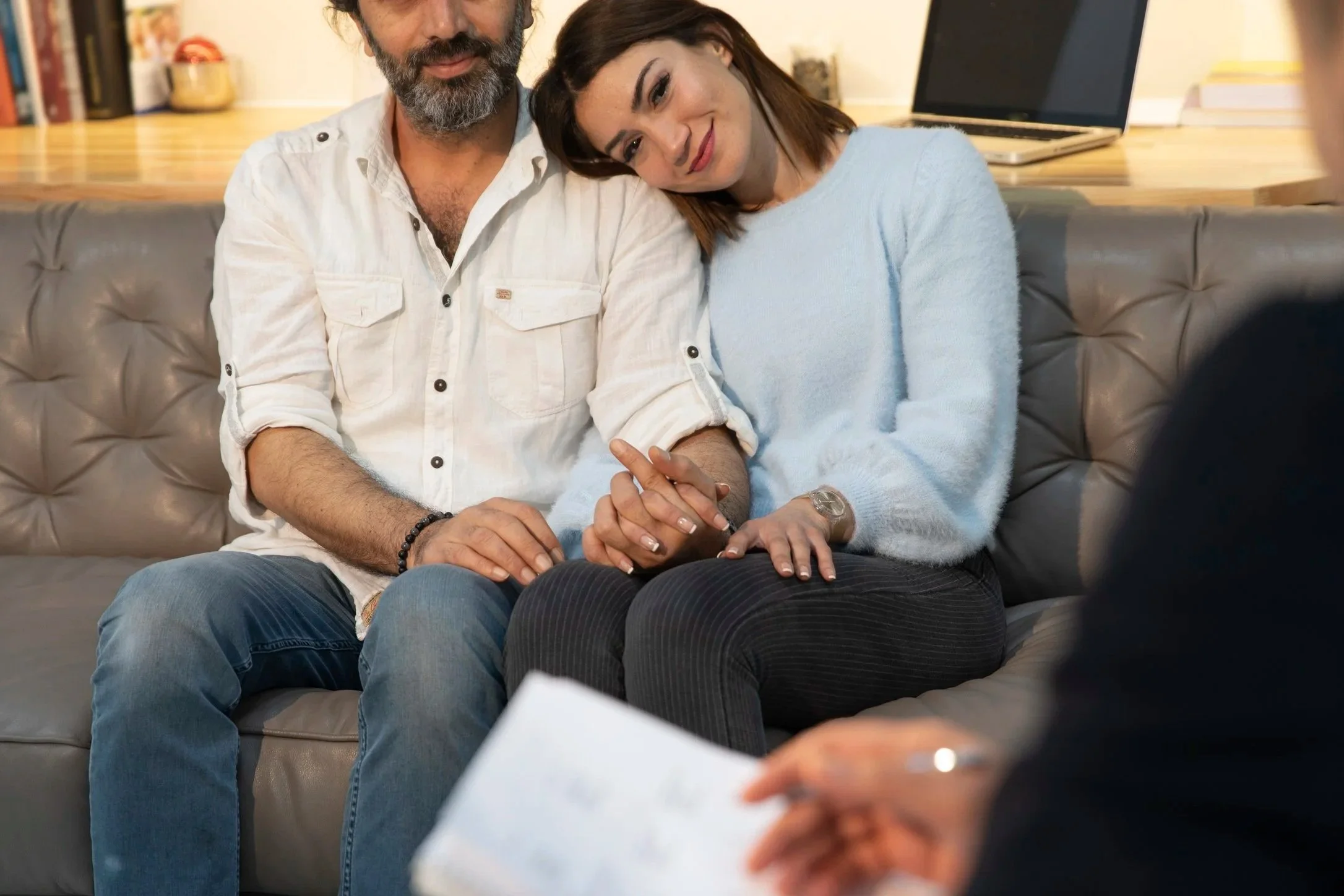 A man and woman holding hands, sitting on a couch during a counseling session.