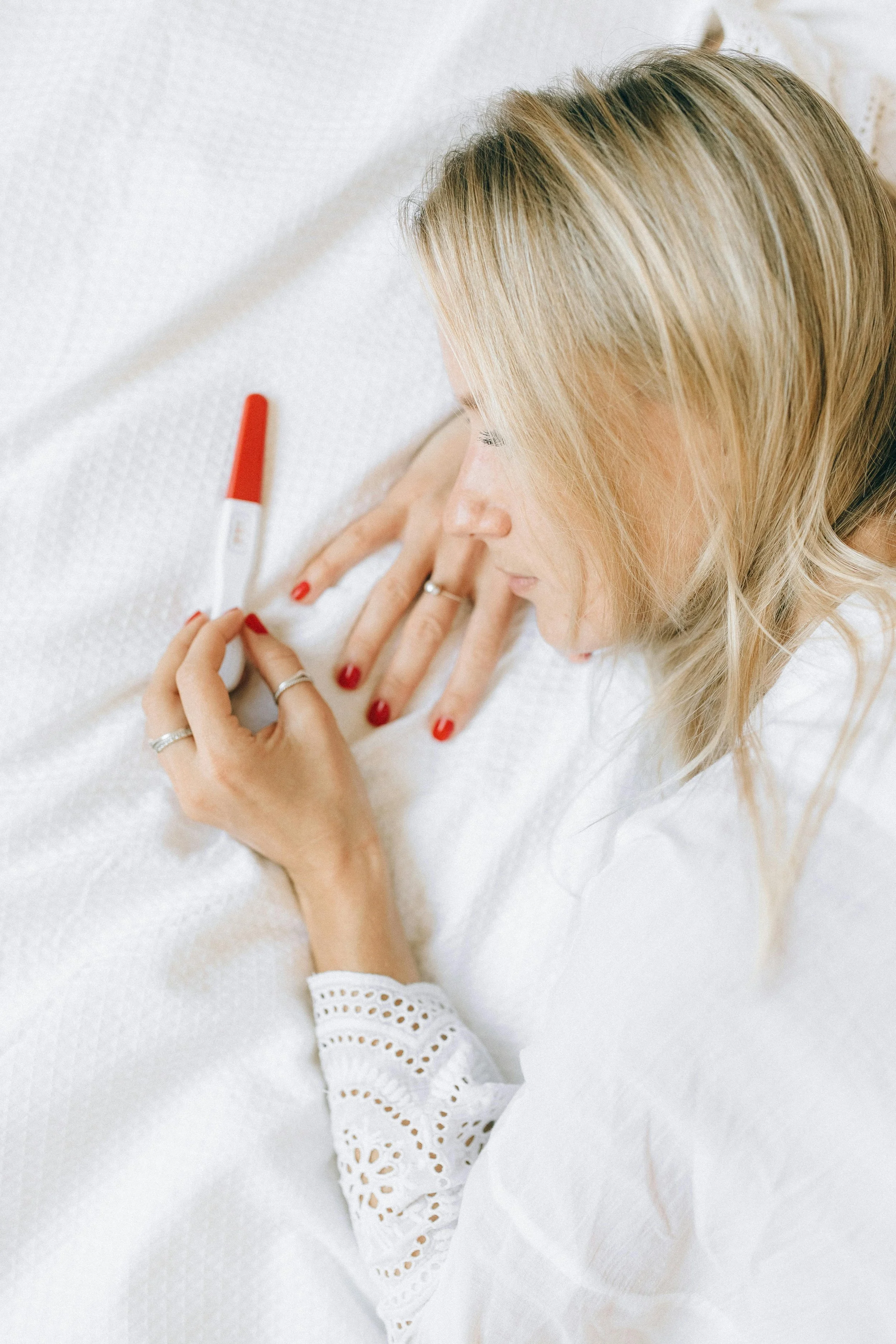 A woman with blonde hair, lying in bed, holding a positive pregnancy test.