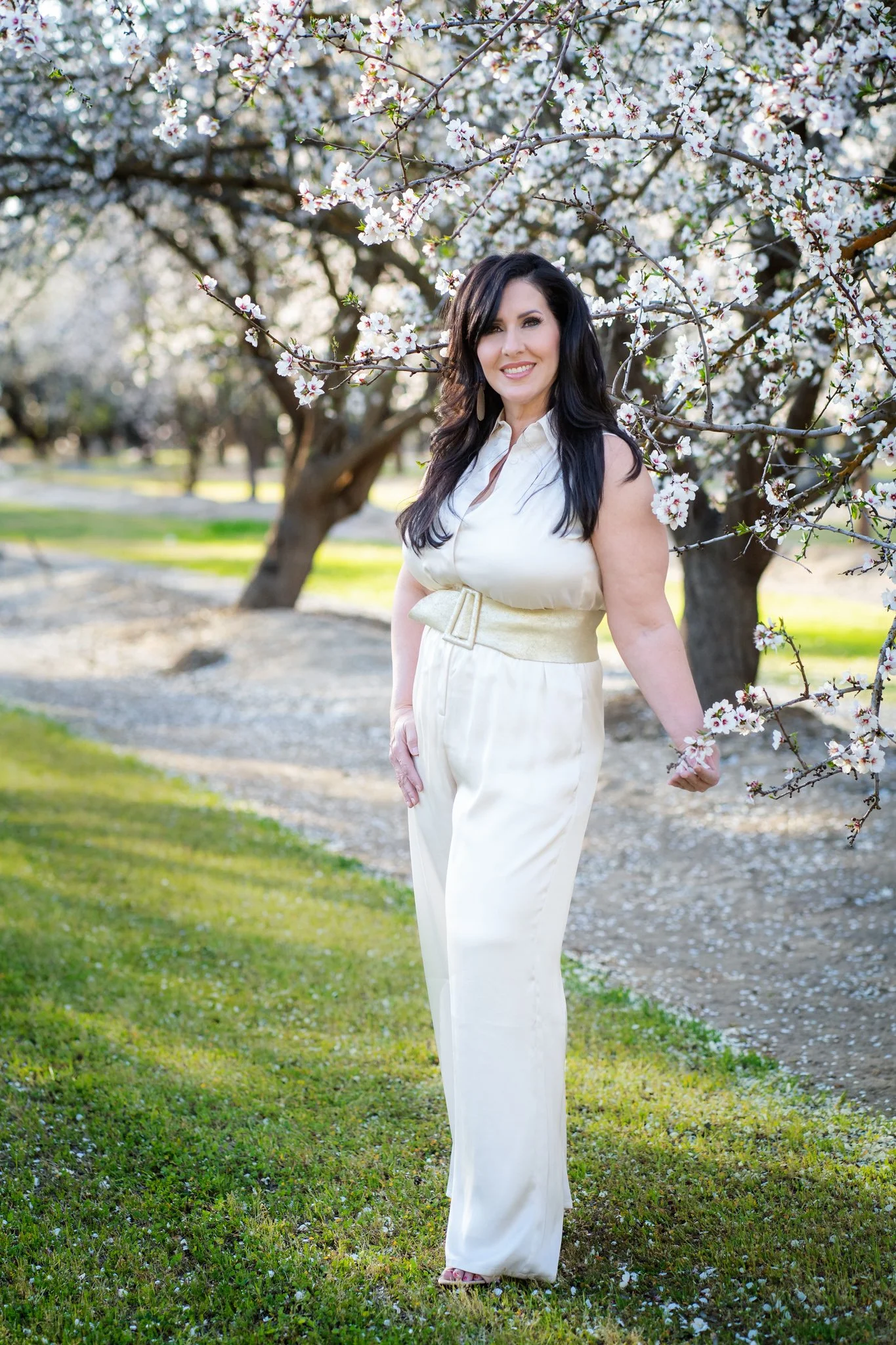 Veronica Cardona standing among blooming cherry blossom trees in a park during daytime.