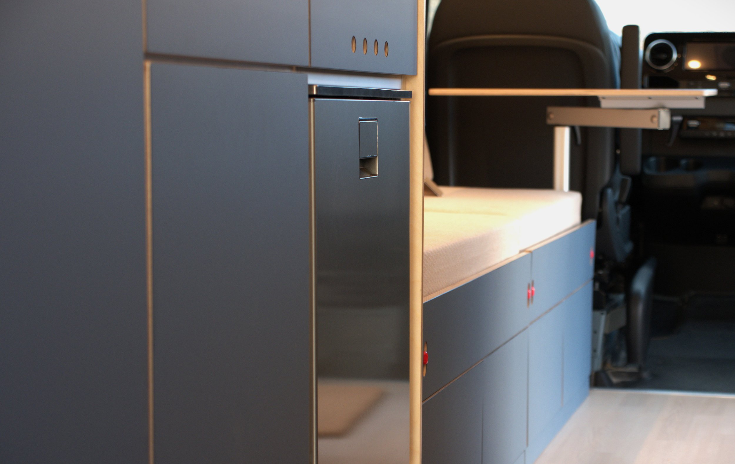 Low-angle interior detail in 'Nordlys' — blue-grey cabinet panels with push-latch hardware, sleeping platform visible, looking through to the captain's seat and cab