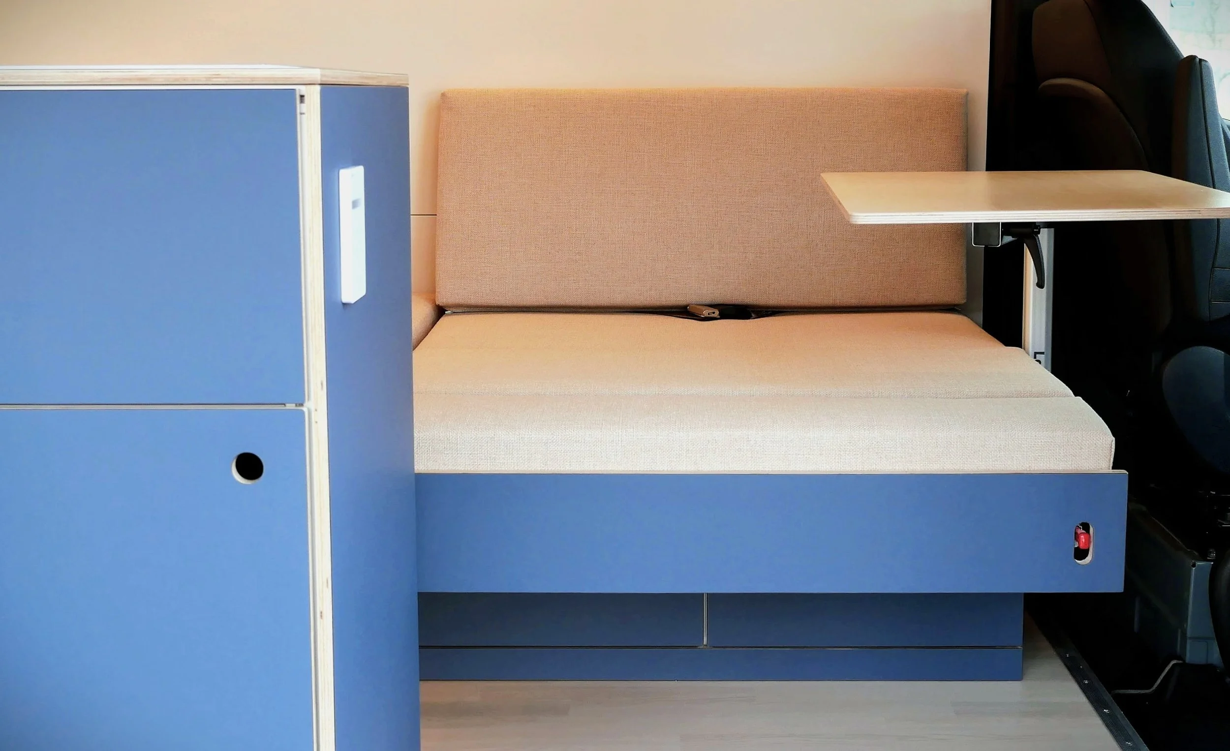 Full sleeping platform deployed in 'Nordlys' — beige cushions extended across the full width, bench backrest raised, Lagun swivel table to one side, blue cabinet and captain's seat visible