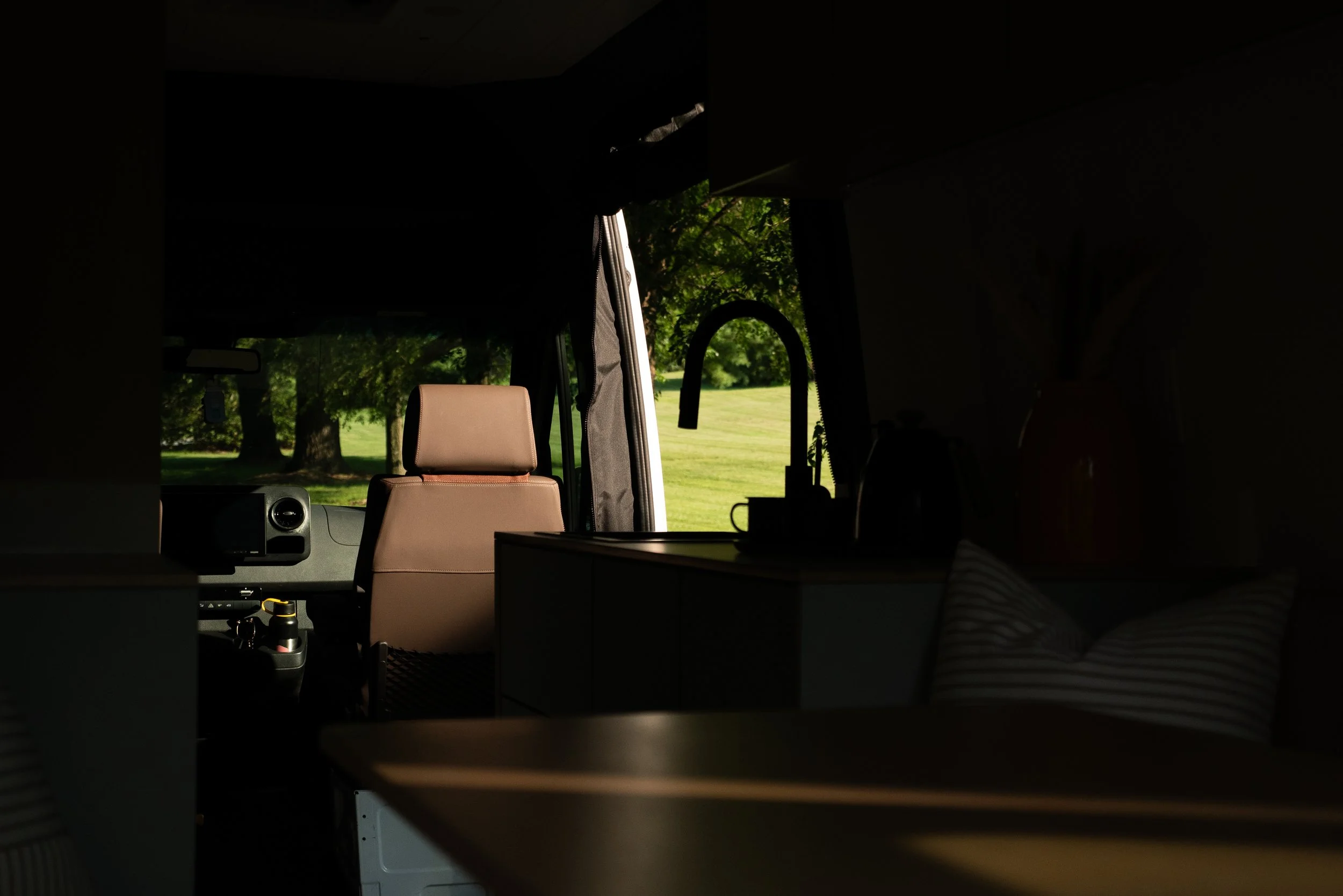 View from the living area toward the cab in 'Aina' — black gooseneck faucet silhouette, dark wood countertop, and open sliding door with green landscape beyond