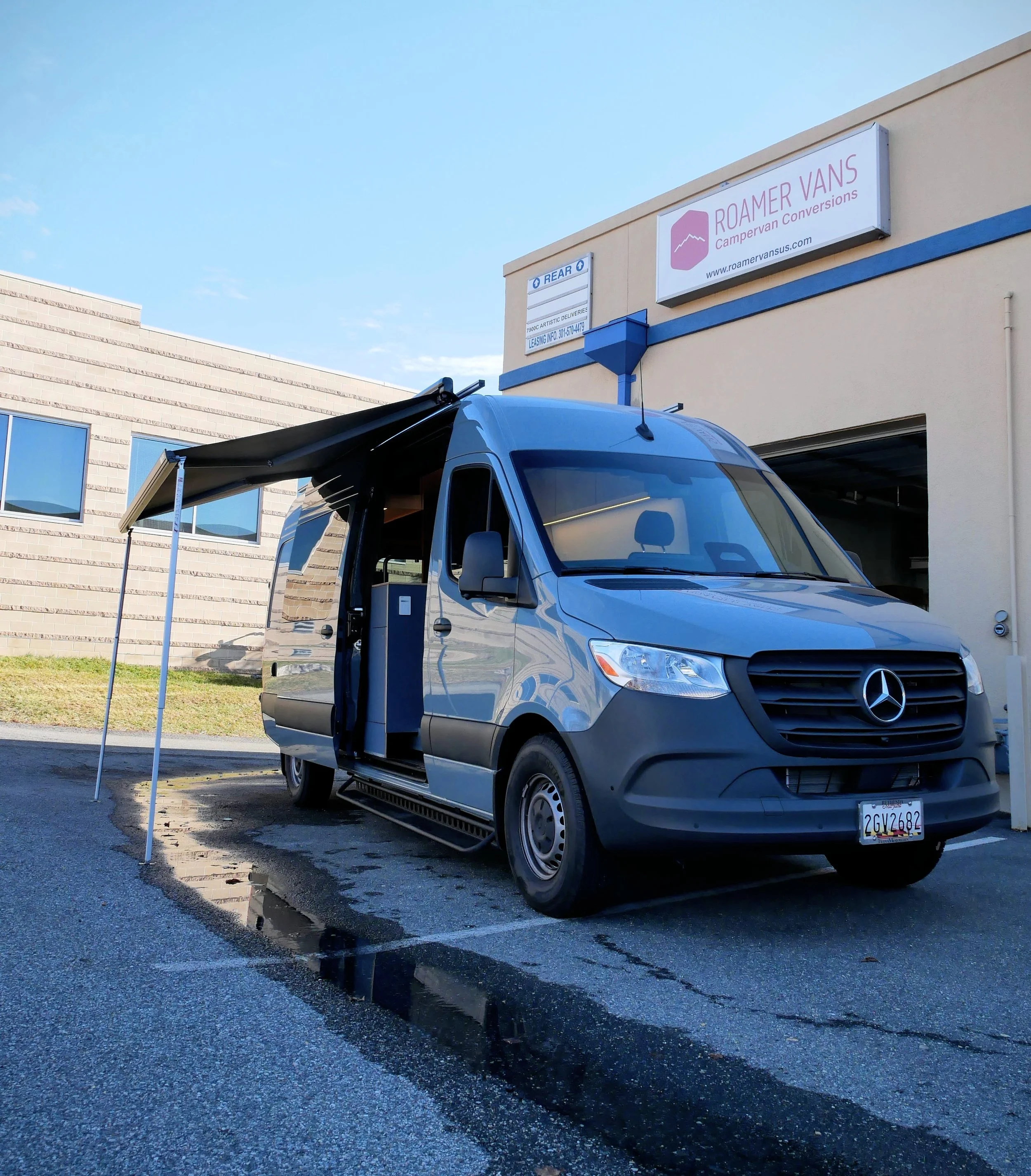 Nordlys' custom Mercedes Sprinter campervan conversion outside the Roamer Vans build facility in Maryland — grey van with awning deployed and sliding door open