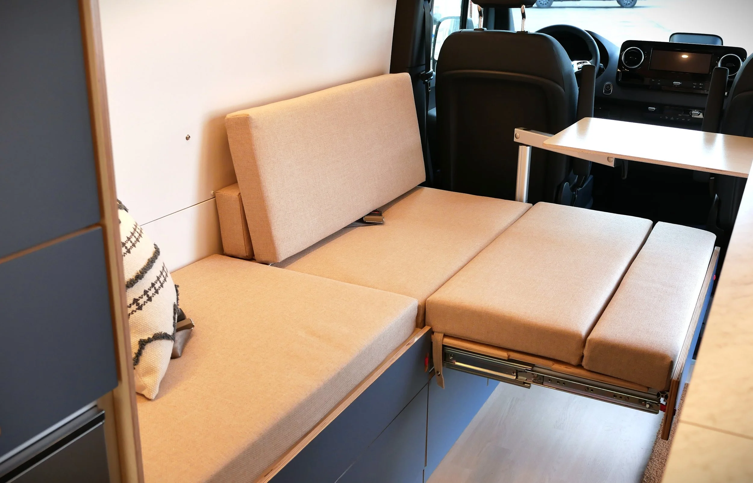 Bench-to-bed conversion in 'Nordlys' — pull-out section extending to meet the fixed bench to form the full sleeping platform, van cab and captain's seat visible beyond