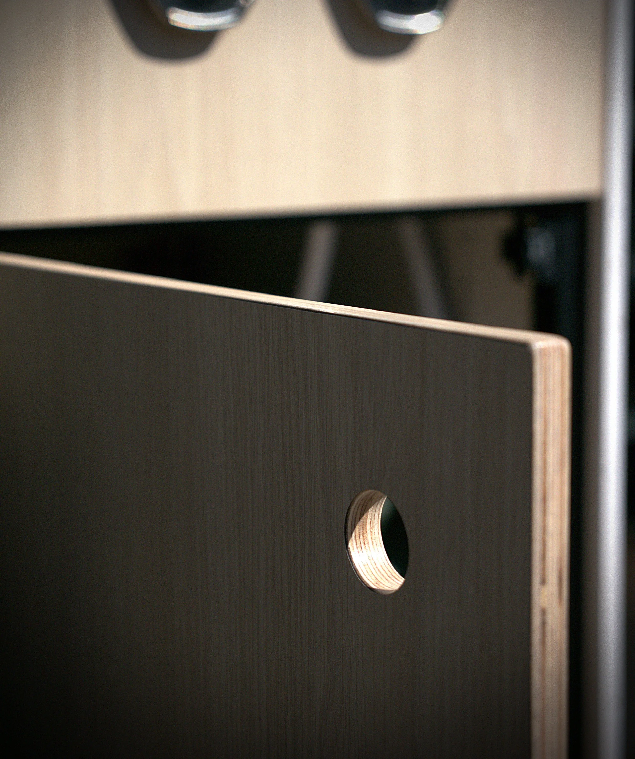 Custom van conversion cabinetry detail in 'Bjorn' — light wood laminate face with a routed circular finger pull exposing the natural birch plywood layers beneath, contrasting against the light veneer cabinet above.