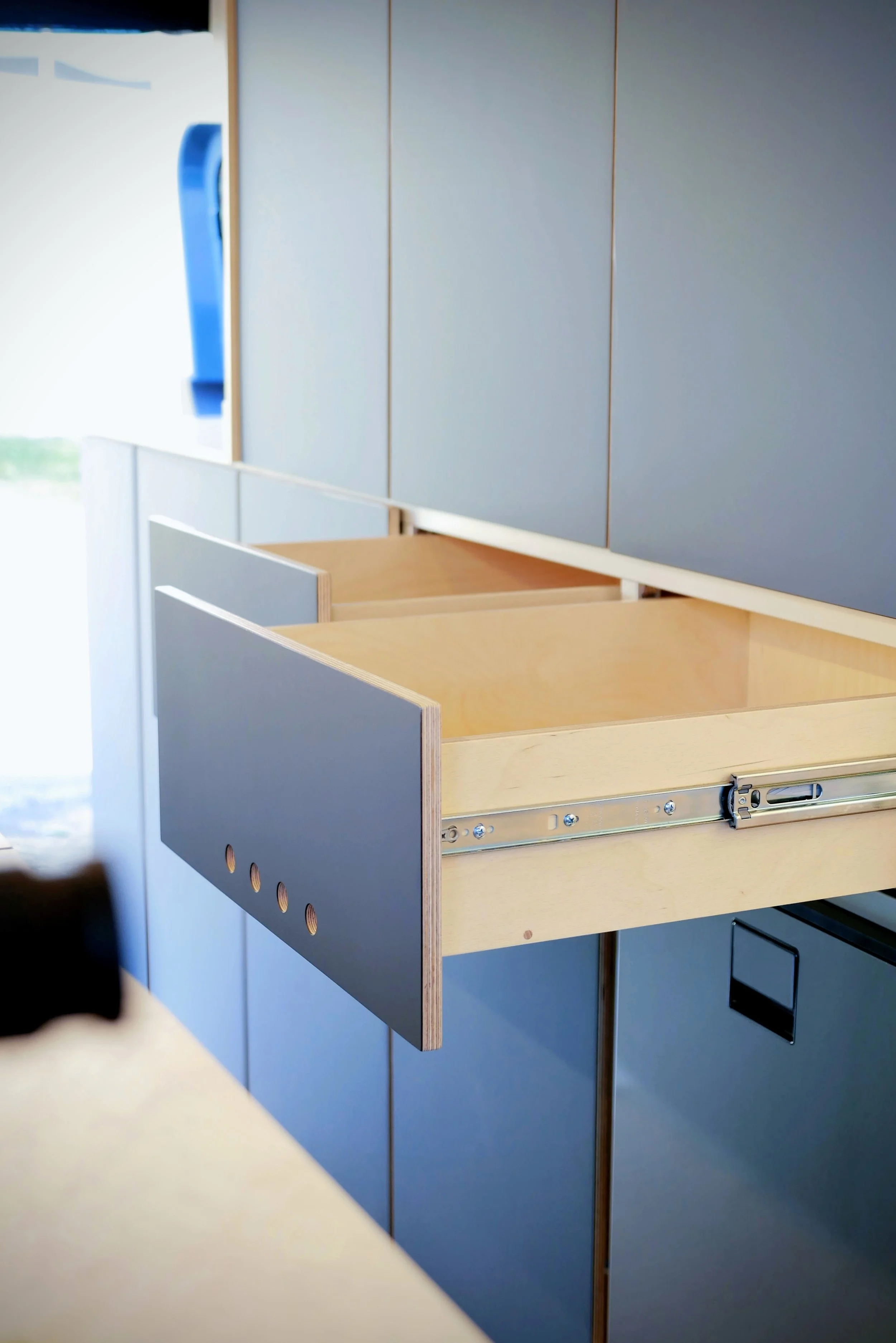 Custom storage drawer in 'Nordlys' — blue laminate-faced plywood drawer on full-extension slides with birch plywood interior, adjacent blue cabinet panel