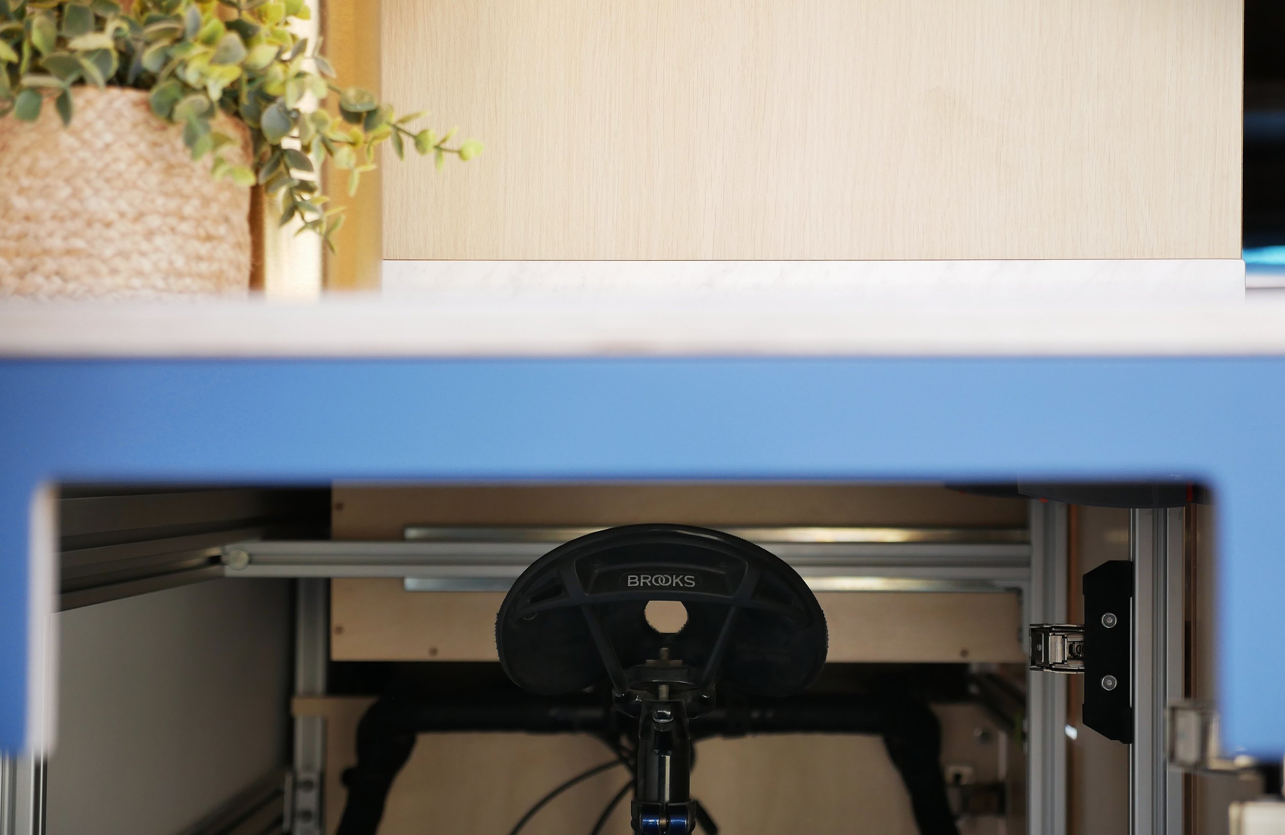 Hidden bicycle storage in 'Nordlys' — bike frame visible in the recessed under-counter slide-out compartment, cleverly concealed within the blue cabinetry