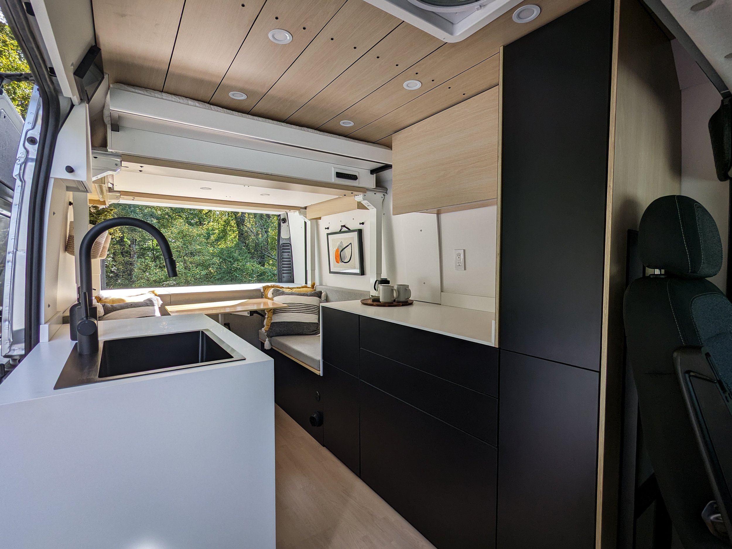 Interior of Roamer Vans Signature Series Koselig campervan conversion — kitchen, dark cabinetry, and bench lounge