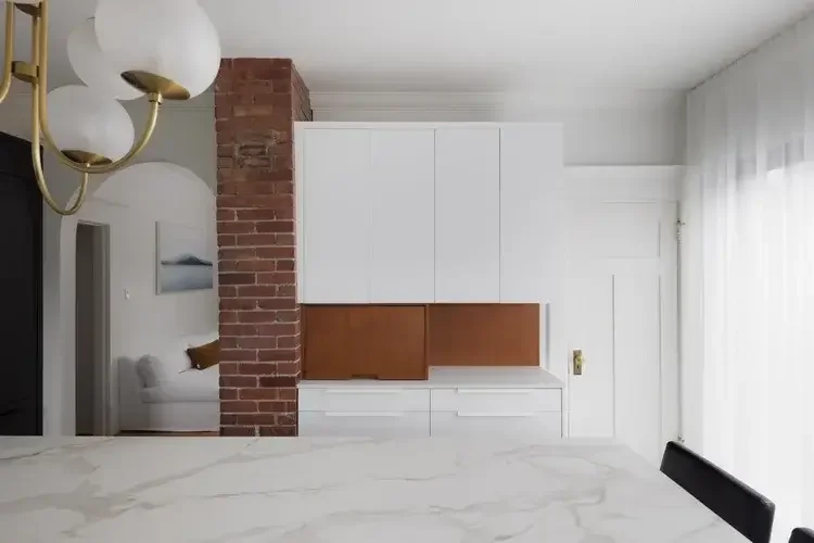 A modern kitchen featuring white cabinets and a rustic brick wall, creating a stylish and inviting atmosphere.
