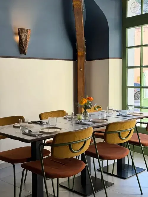 A restaurant interior featuring a table and chairs positioned near a large window, allowing natural light to enter.
