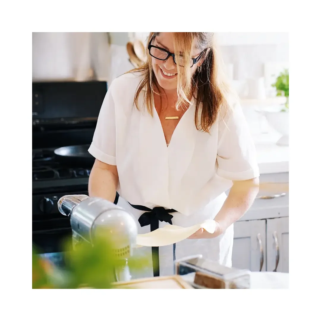 A woman wearing glasses smiles while preparing pizza in a kitchen setting
