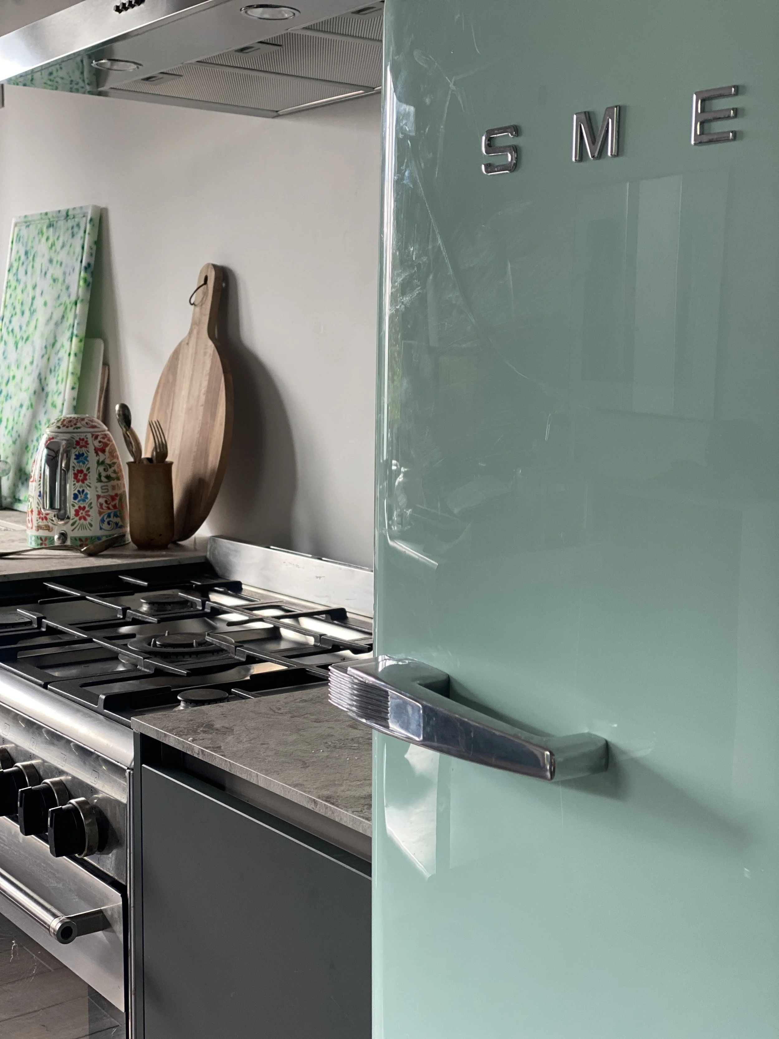 A kitchen scene with a stove, cutting board, teapot, and a mint green refrigerator with metallic handles.