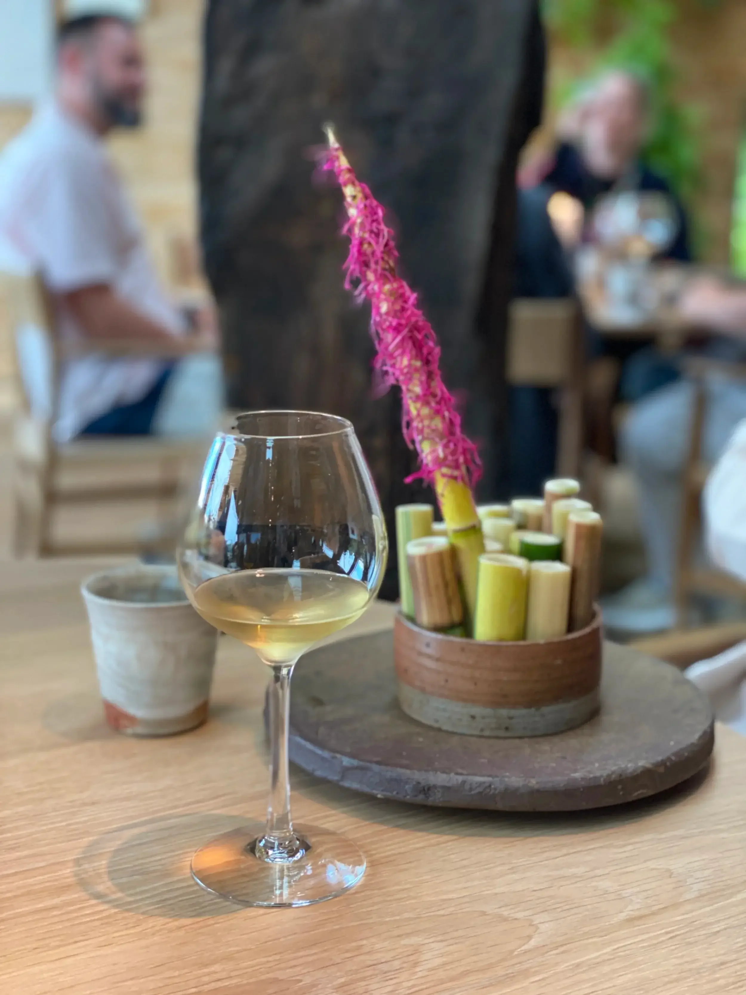 A glass of red wine beside a bowl of pasta on a wooden table, creating a cozy dining atmosphere.