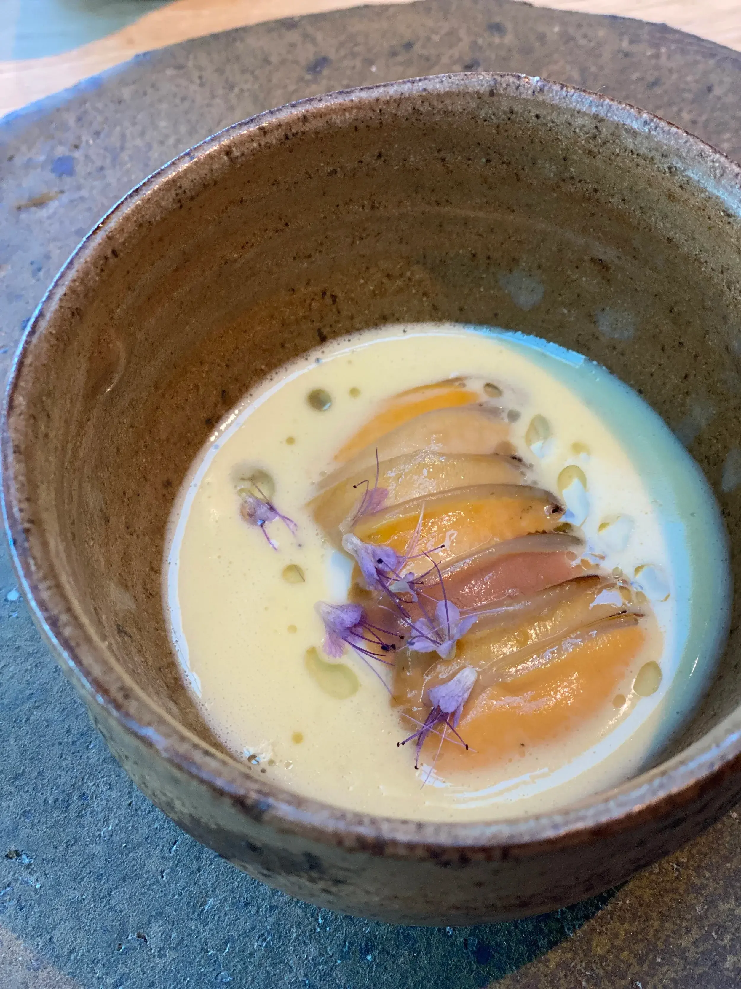 A bowl of soup featuring a soft-boiled egg nestled in the center, garnished with herbs.