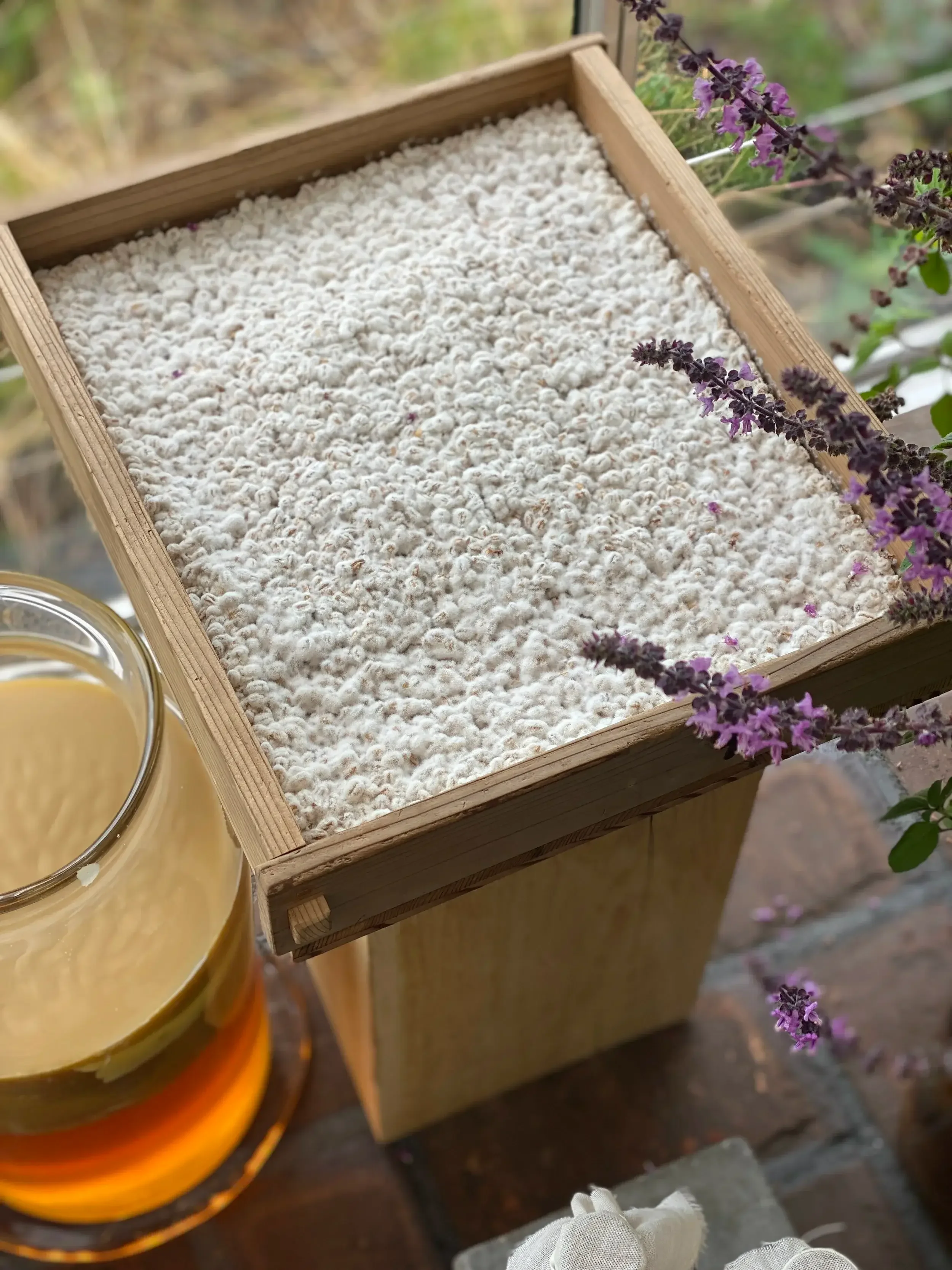 A wooden box holds a glass of water beside a blooming flower, creating a serene and natural arrangement.