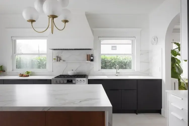 A modern kitchen featuring elegant marble countertops and a spacious white island for cooking and dining.
