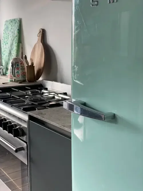 A kitchen featuring a green refrigerator and a stove, showcasing a modern and vibrant cooking space.