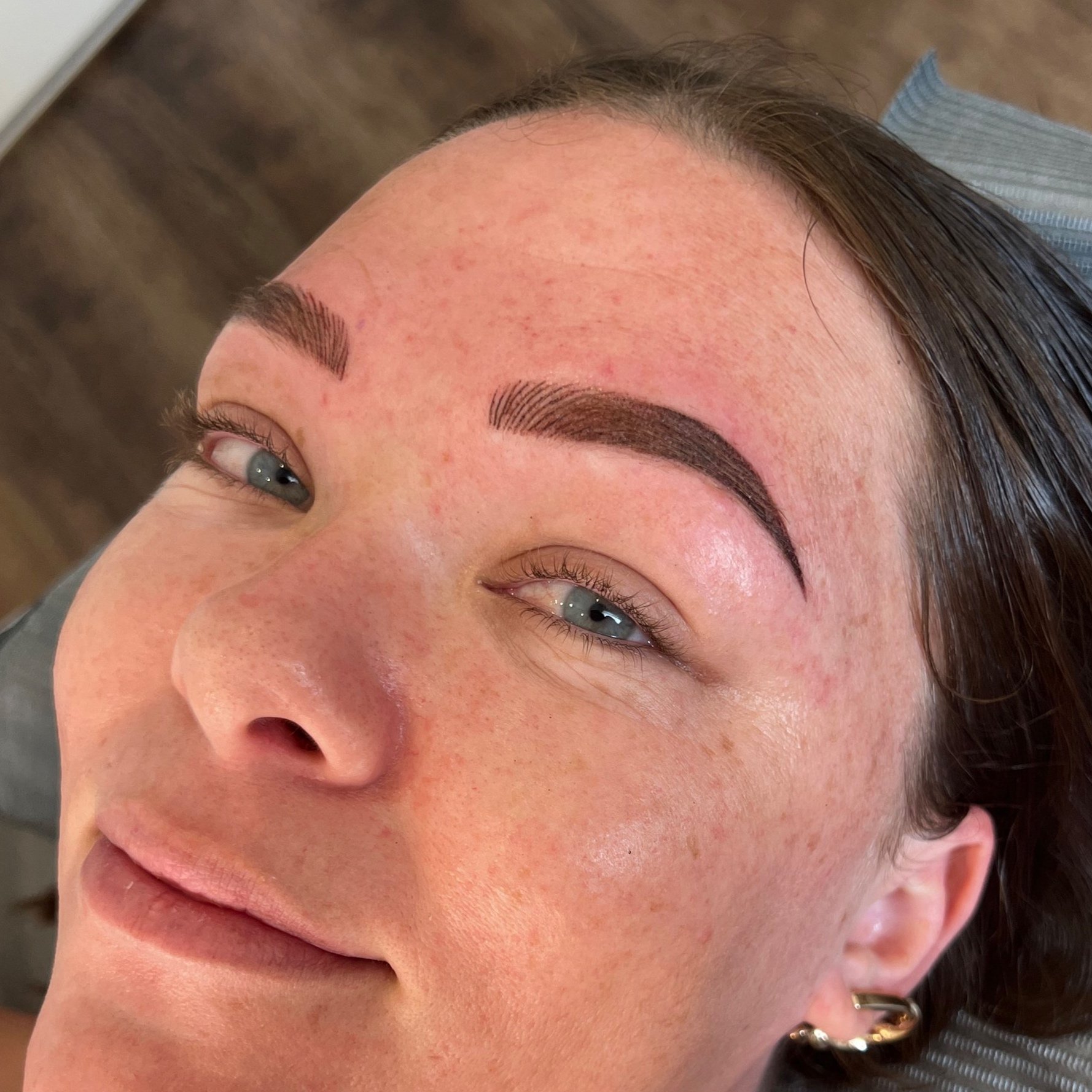 Close-up of a woman with freshly done eyebrow tattoos, showing well-defined, dark arched eyebrows, and smooth skin with some redness. Cosmetic Tattoo Eyebrows