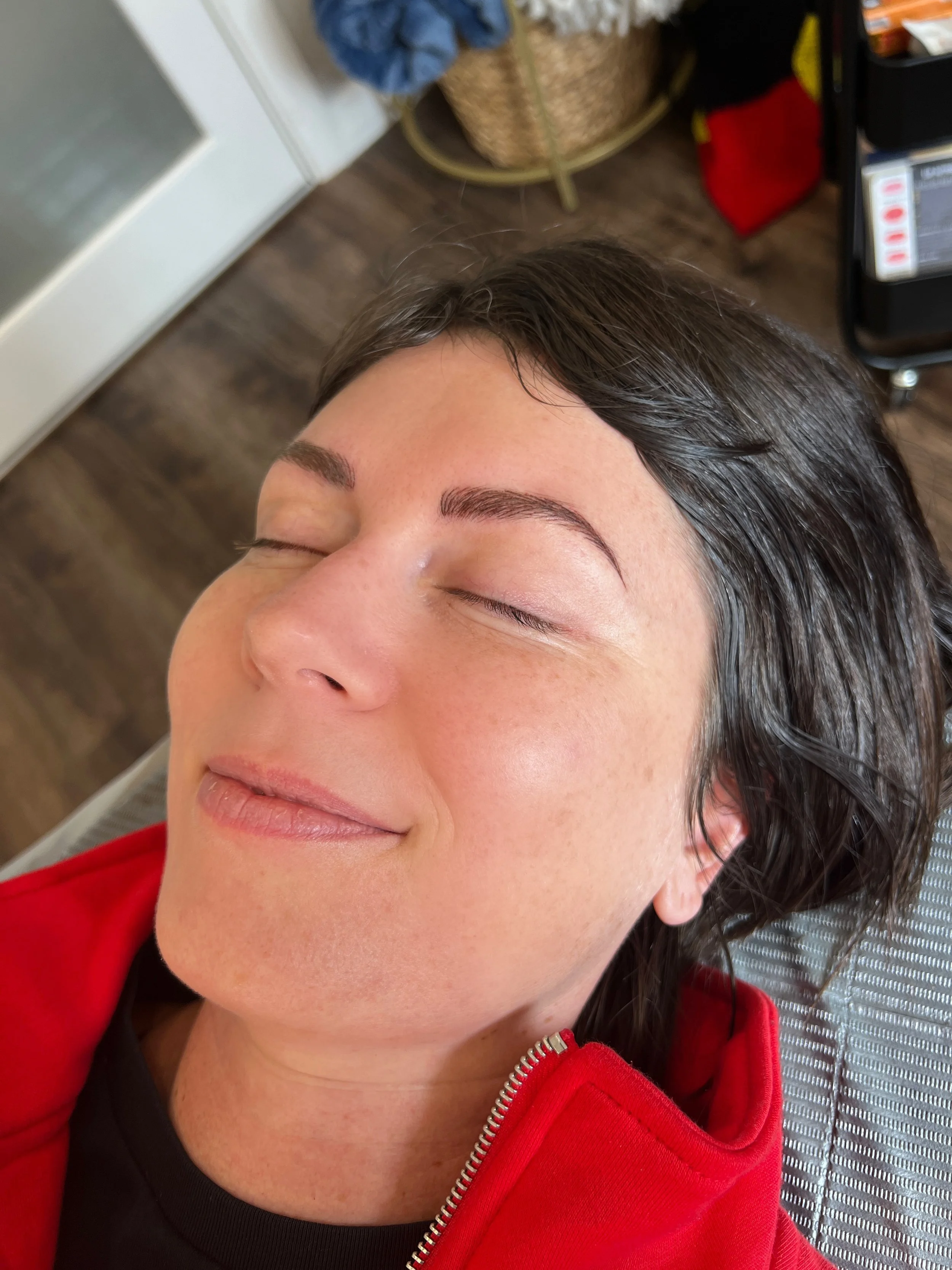 A woman with dark hair, closed eyes, and a gentle smile, resting with her head tilted back, wearing a red jacket.