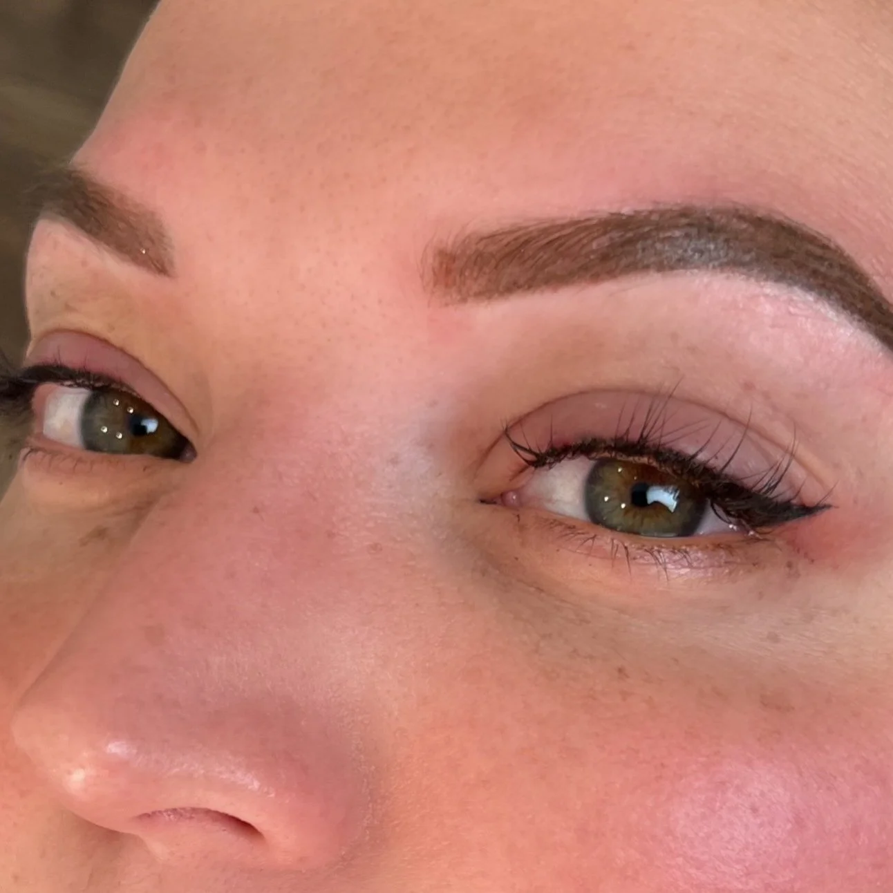 Close-up of a woman's face showing prominently groomed eyebrows, eye makeup, and hazel eyes.
