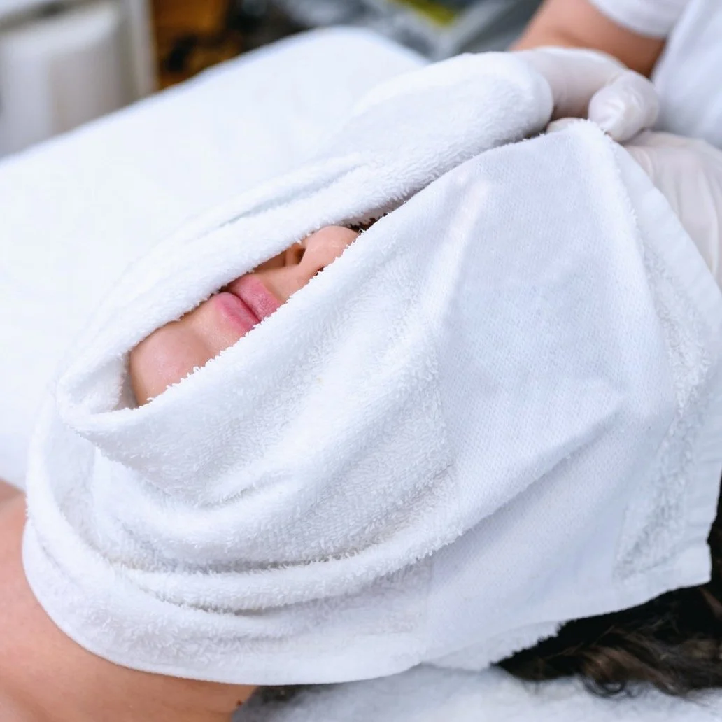 Person lying under a white towel with only their nose and lips visible, being covered by a fluffy white towel or blanket.