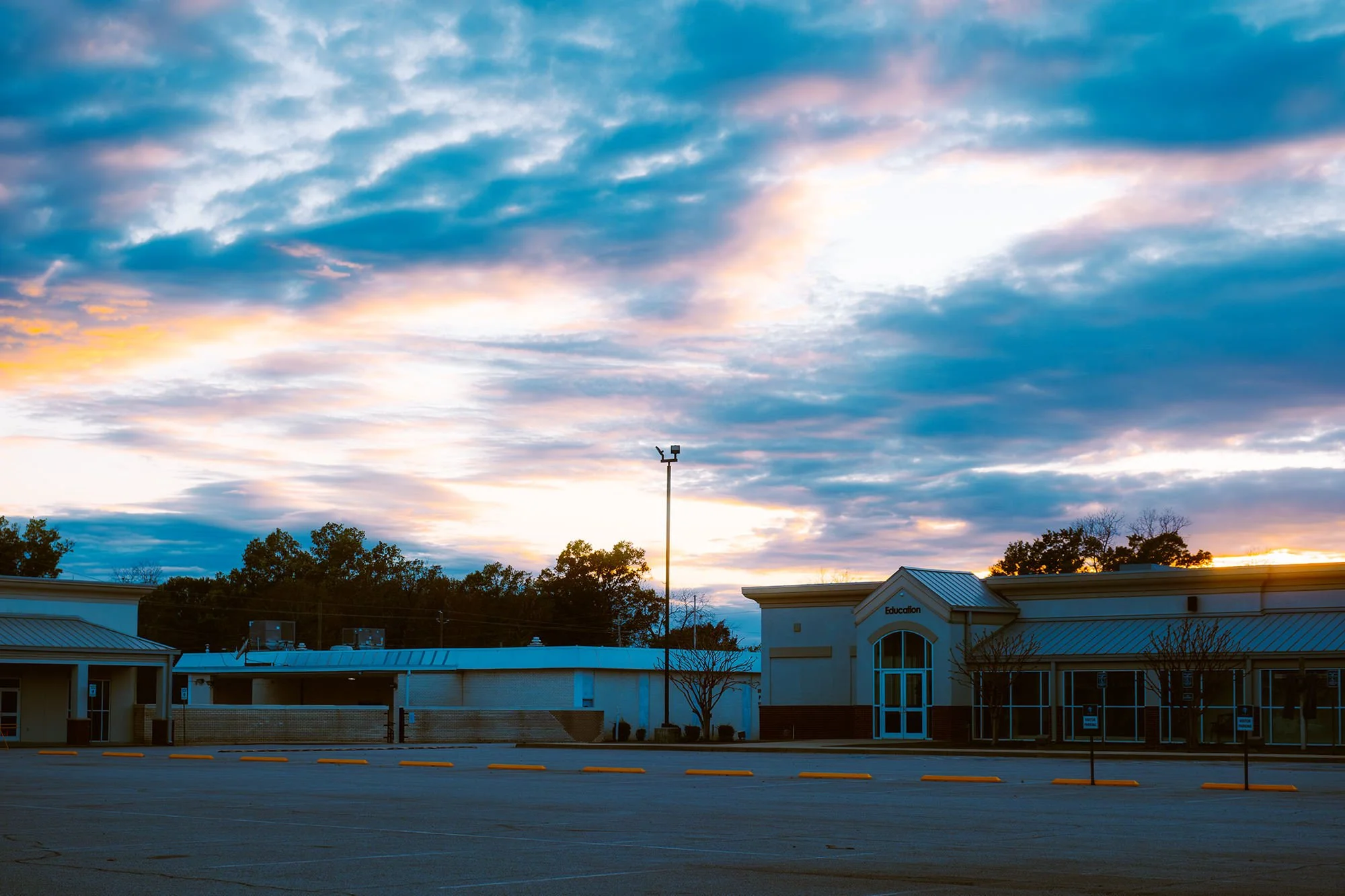An empty school parking lot at sunset with a school building labeled 'Education' and a sky filled with clouds.