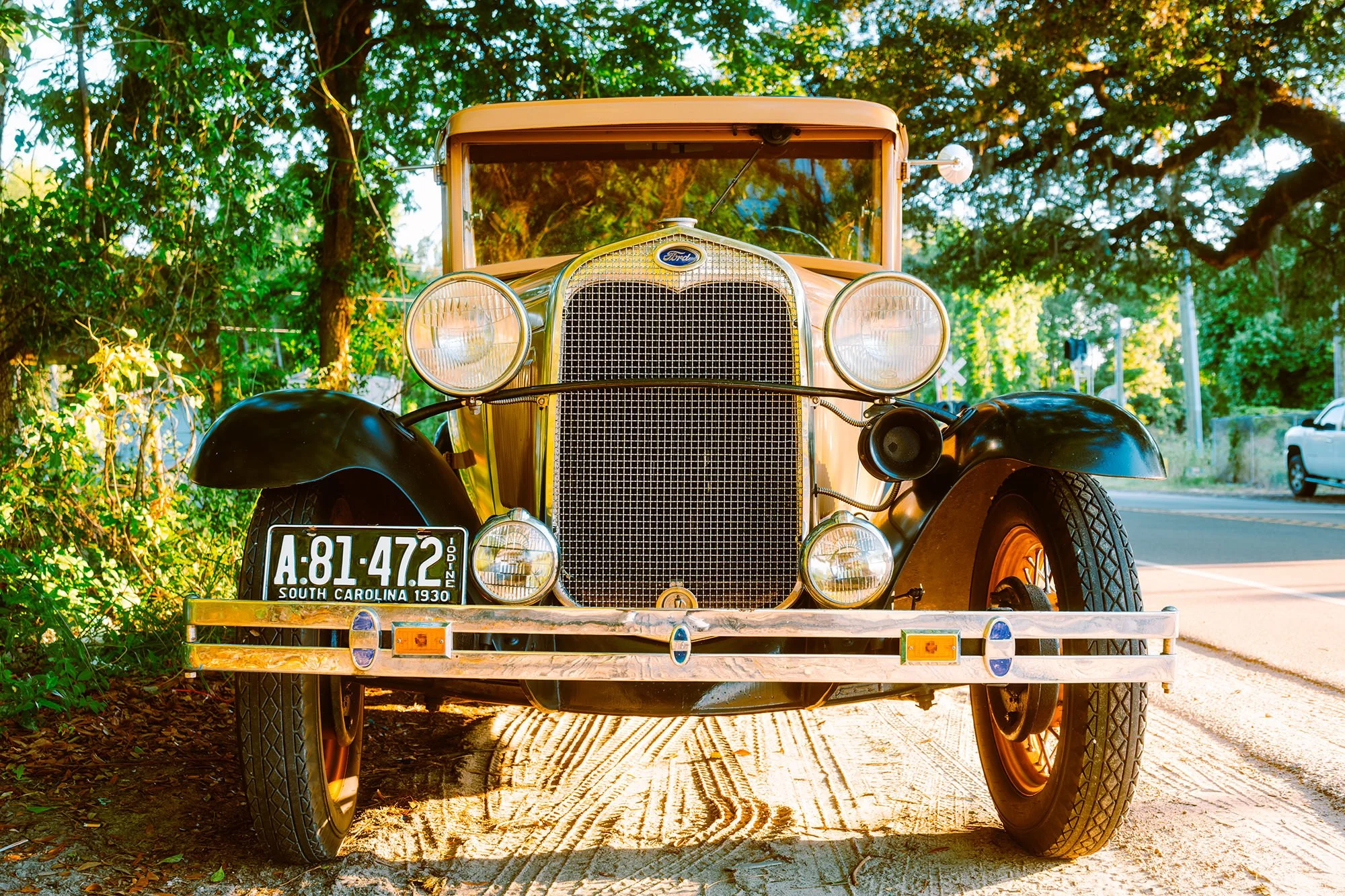 Front view of a vintage 1930 Ford car with South Carolina license plate, parked on a dirt path with green trees in the background.
