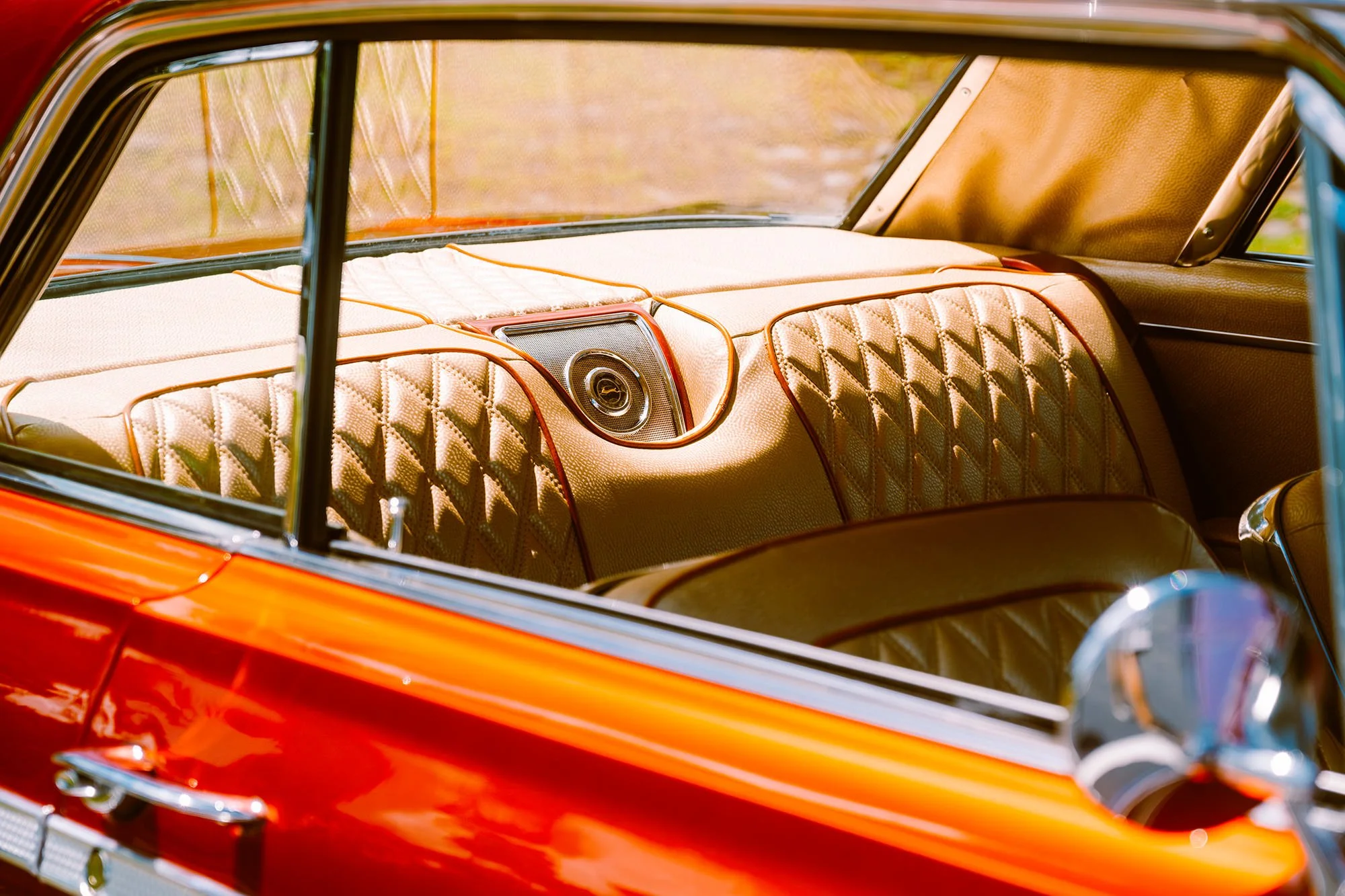 Close-up of the interior of a vintage car with quilted gold upholstery, central speaker, and orange exterior paint.