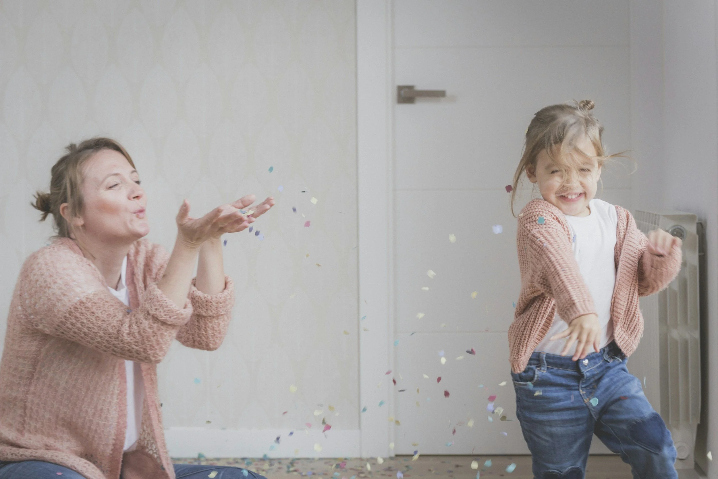 A mother who is wearing a piknk cardigan, white t-shirt, and blue jeans enjoying confetti with her daughter who has a matching outfit