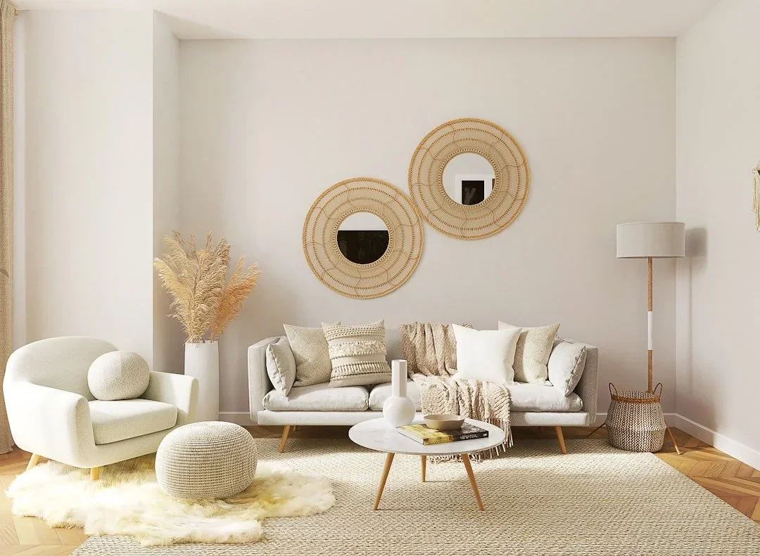 A living room with different variations of beige items including a sofa, armchair, ottoman, coffee table, mirrors, blankets, pillows, flowers, and rugs.