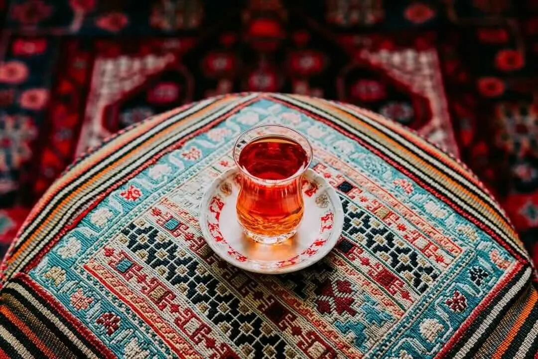 A glass of tea on a decorative, colorful woven tablecloth with a patterned background.